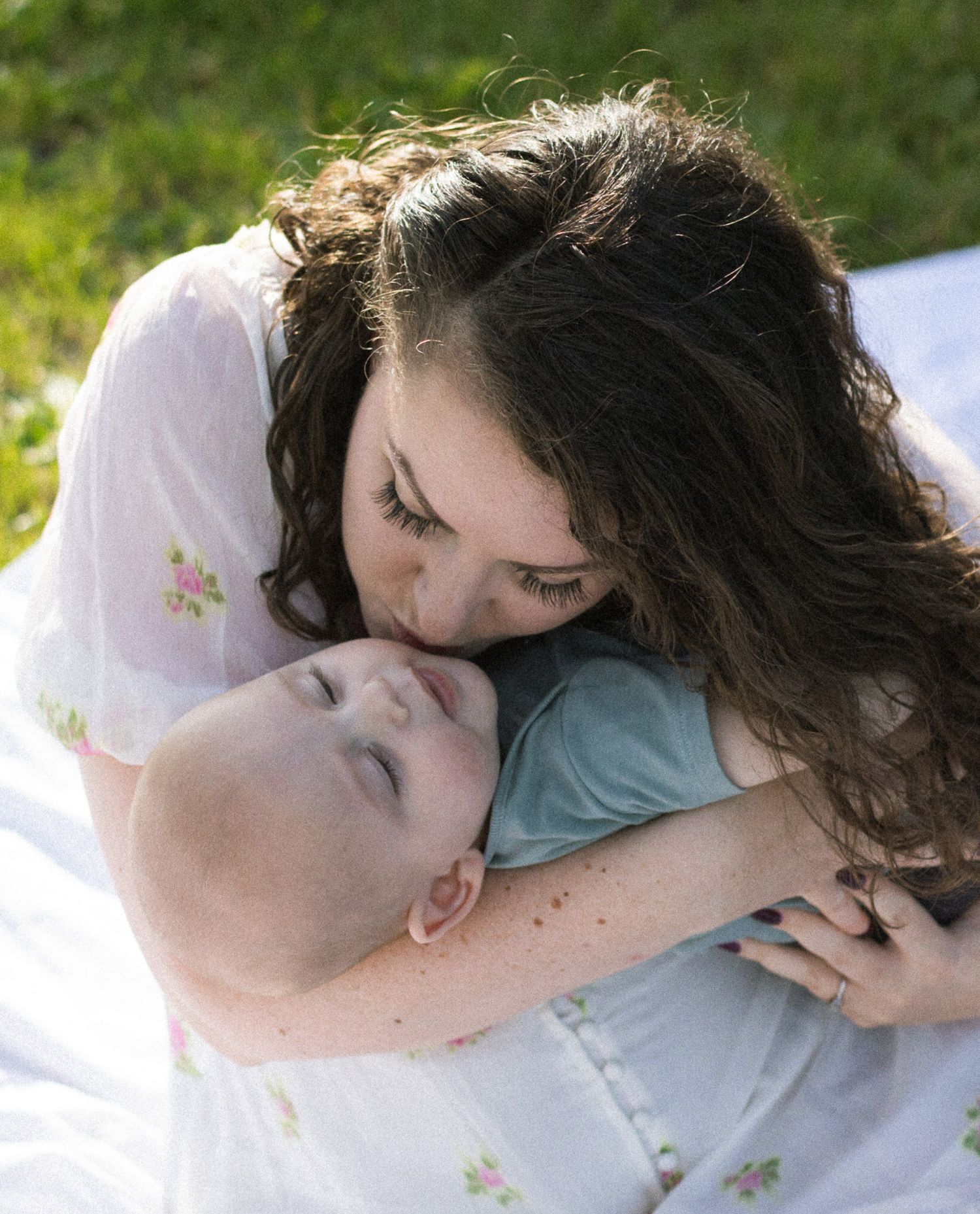 A mother and son shares a kiss while lying down on a white surface.