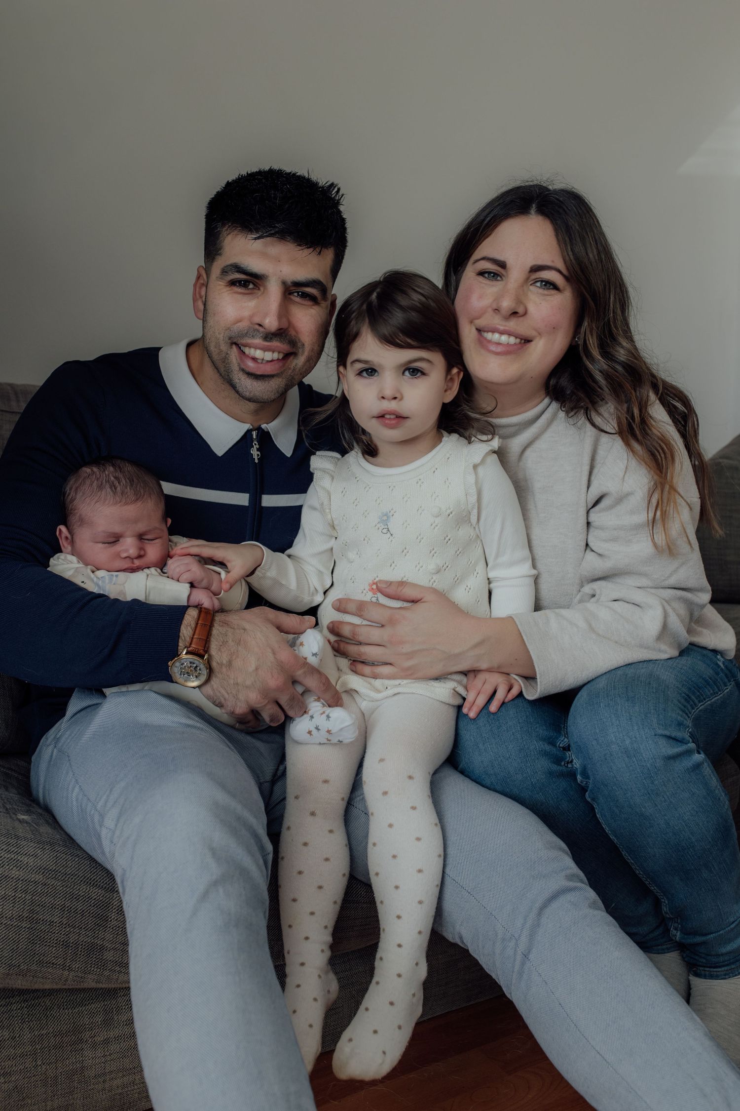 A family wearing casual clothes sits together on a gray couch in a series of intimate portrait photos.