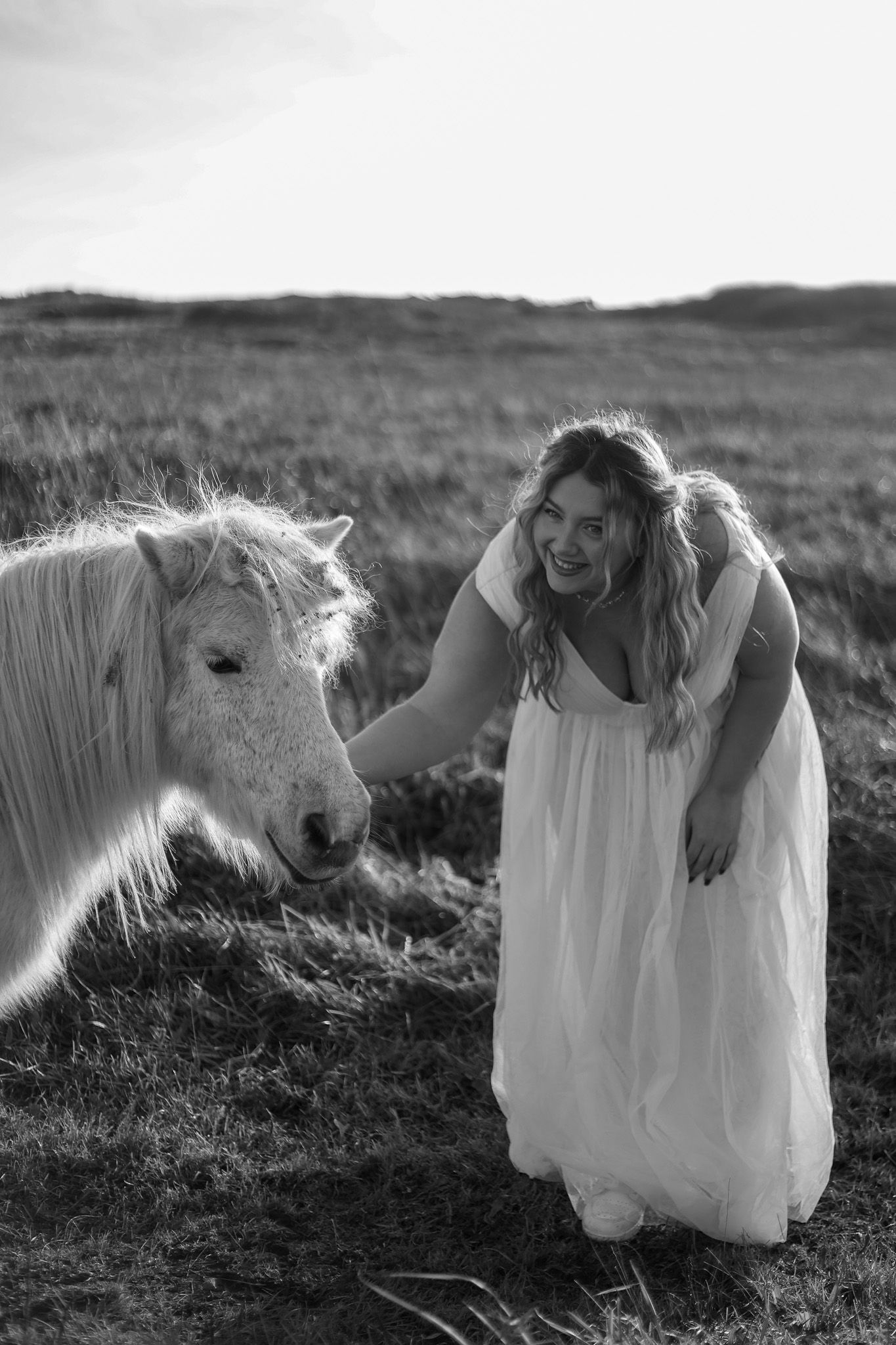 A series of four artistic black and white photos showing a person in a flowing white dress lying in a grassy field.