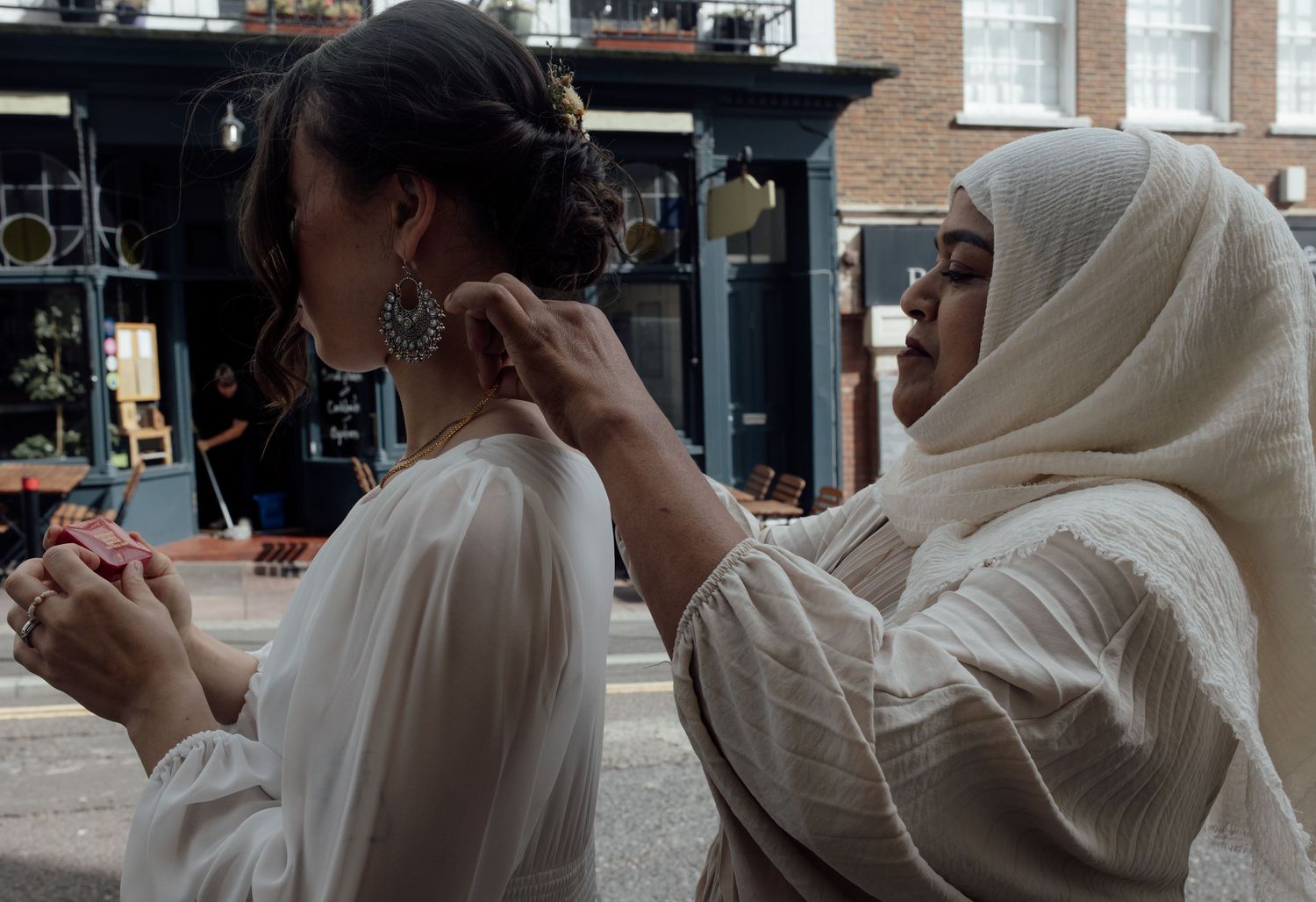 A person in a white dress and veil puts a necklace on in urban background