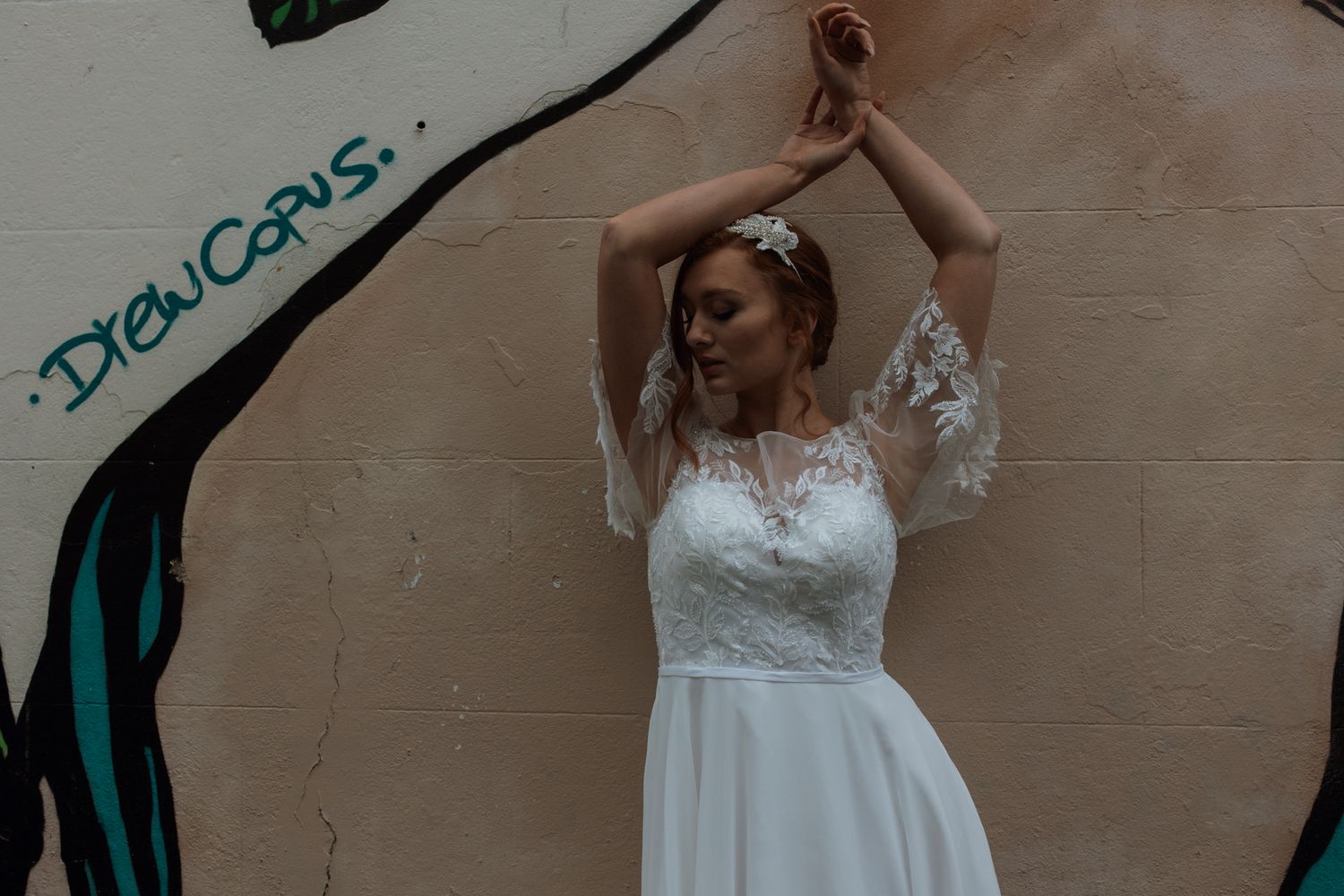 Bride in lace gown with strapless sweetheart neckline poses against textured gray wall.