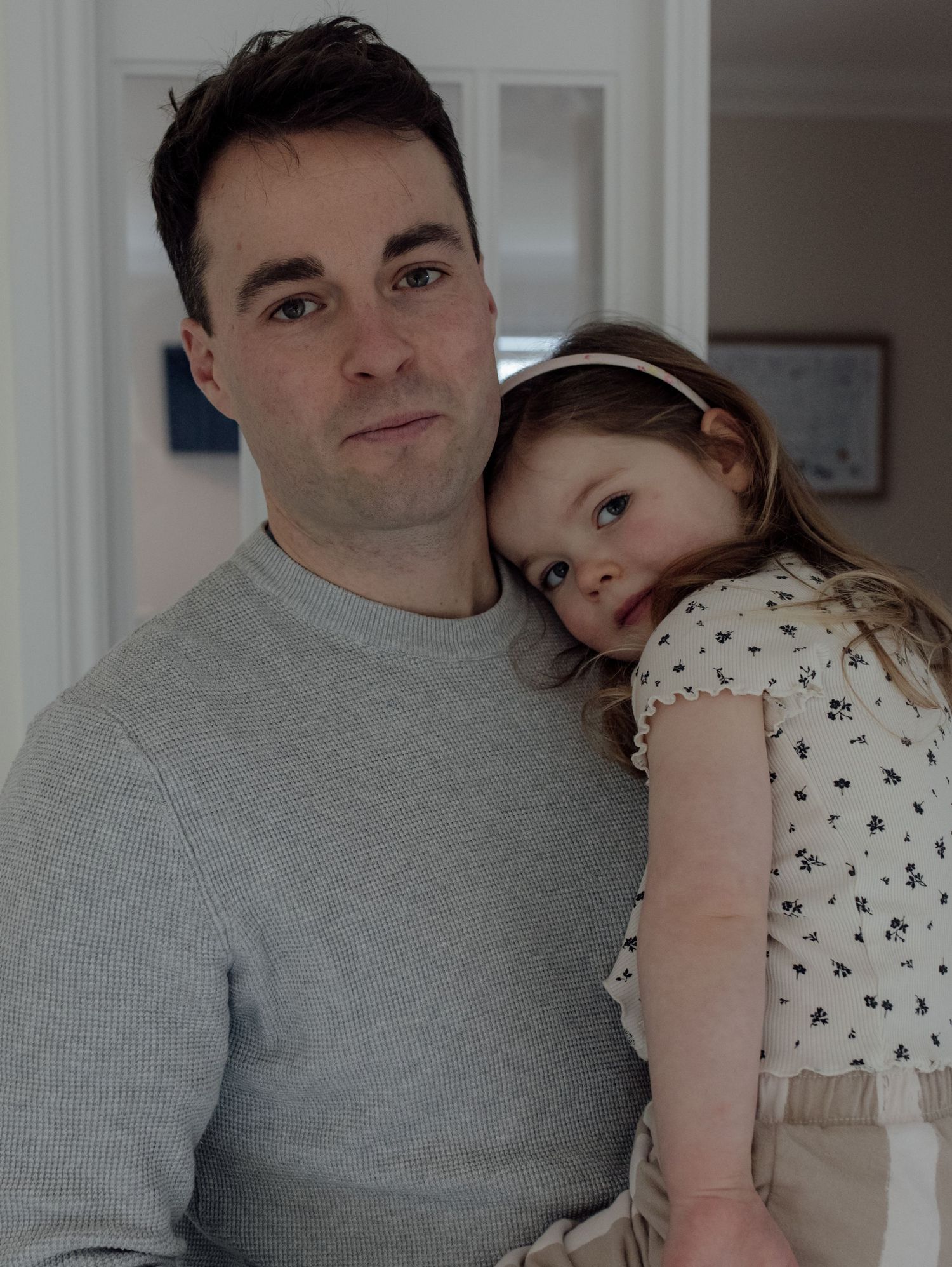A tender moment shared between two people embracing in a white room with a polka dot dress and grey sweater.