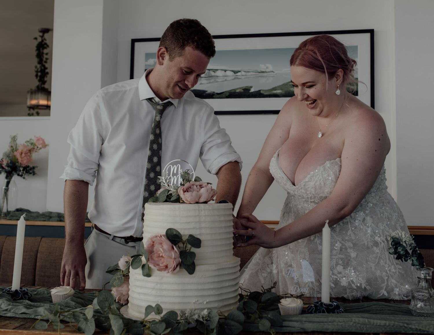 A couple cuts into their elegant white wedding cake together during their reception celebration.