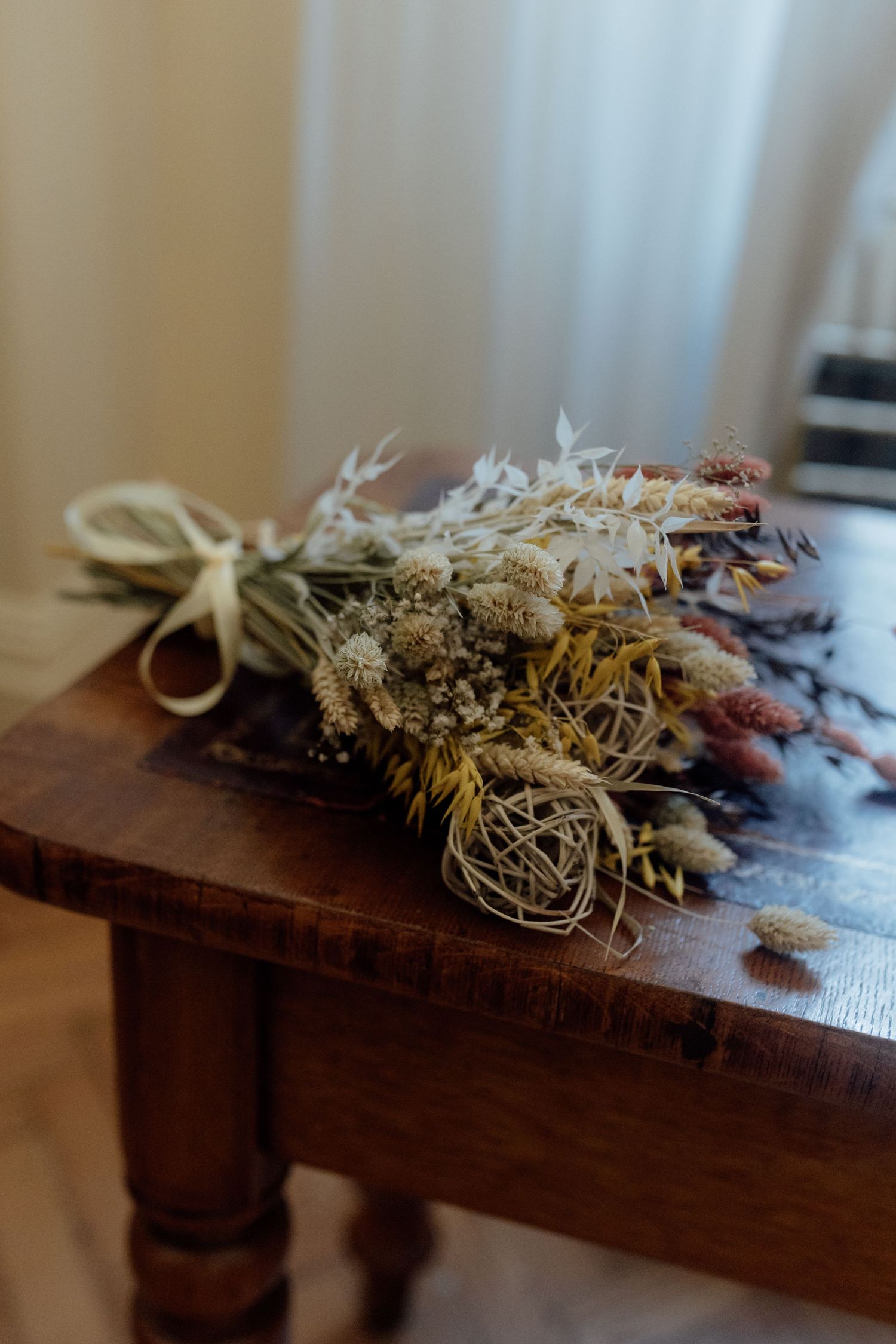 Dried floral arrangement with wheat stalks and preserved flowers displayed on a rustic wooden surface.