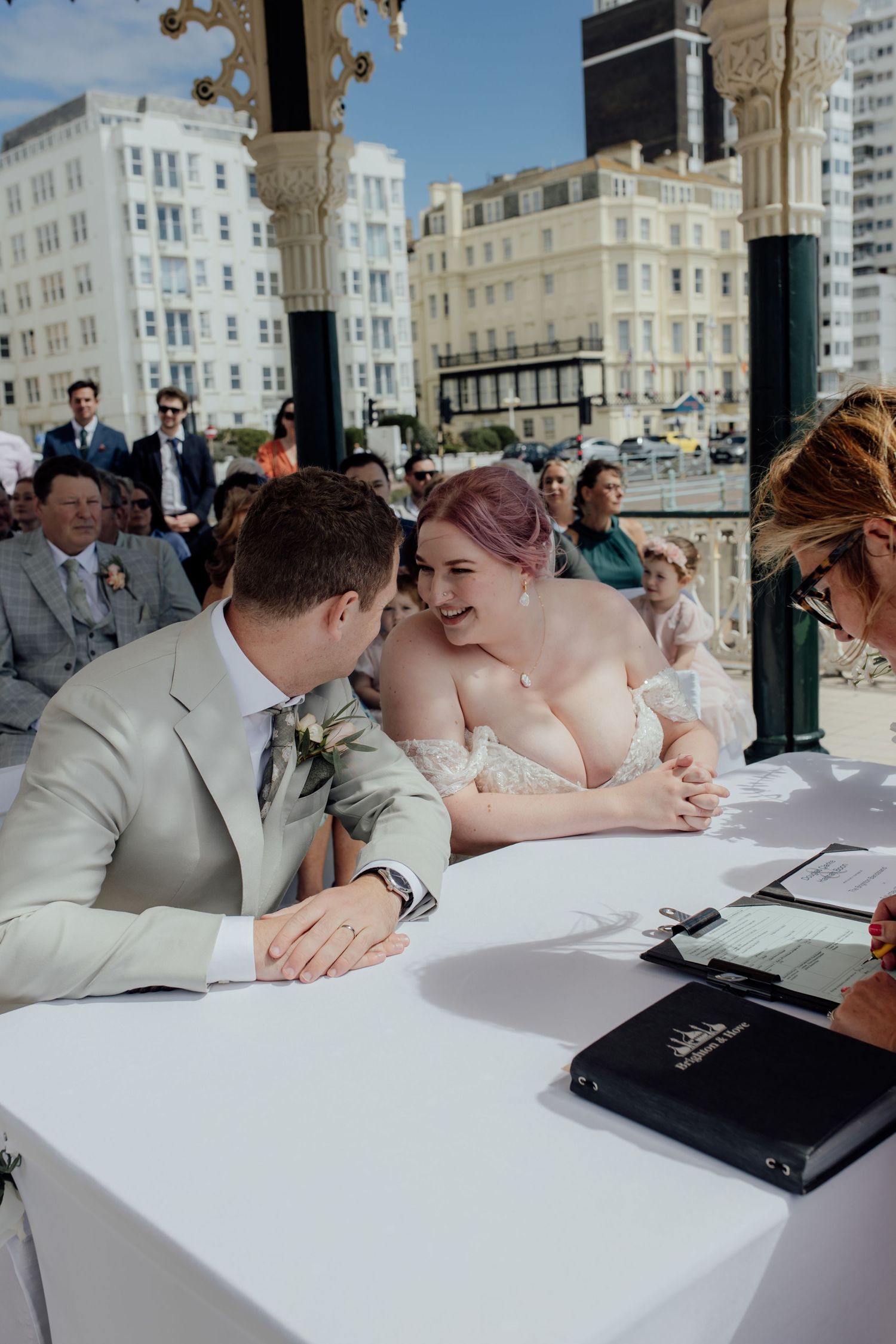 Wedding couple sharing a tender moment while signing documents at a seaside venue.