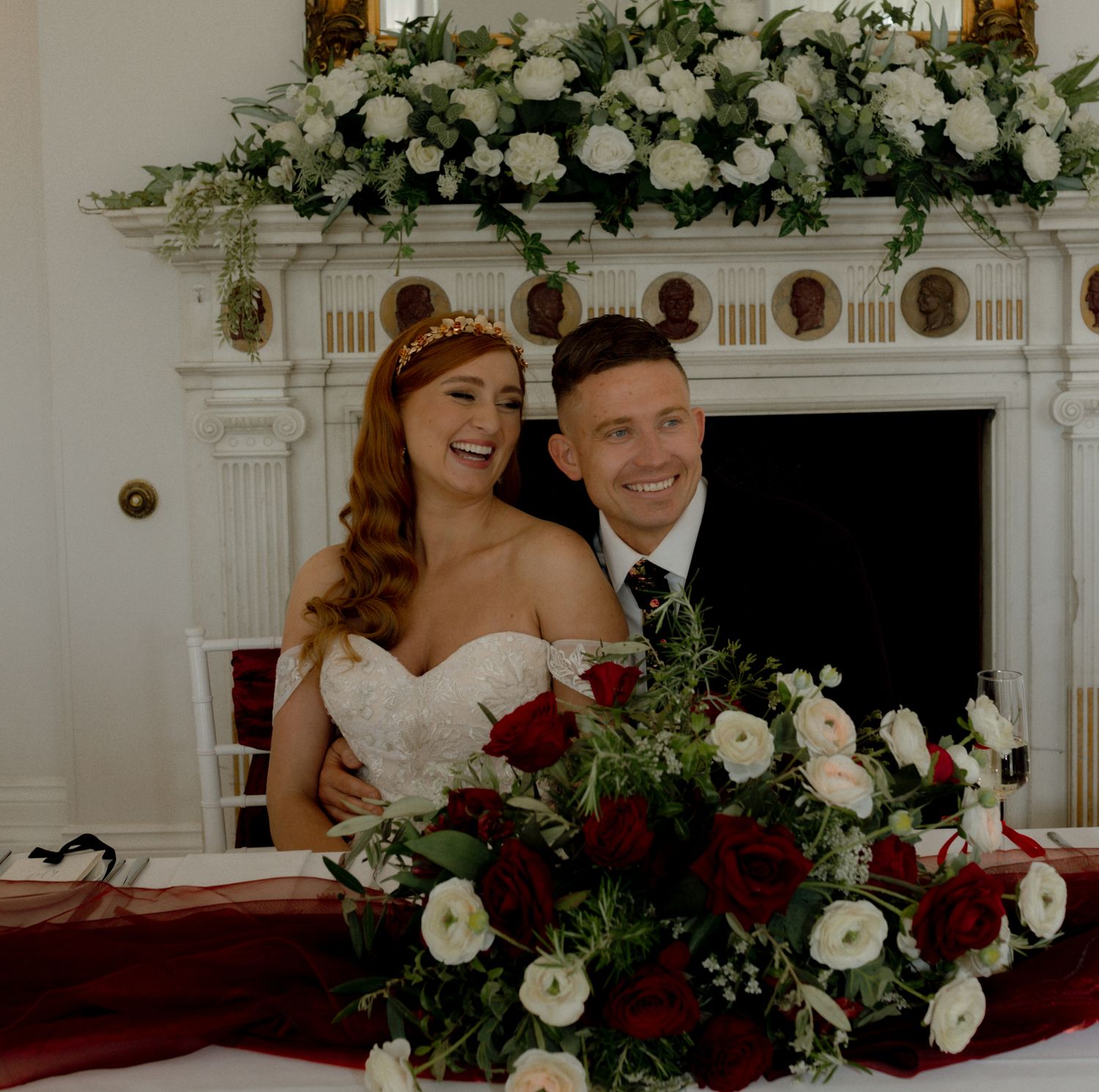 An elegant wedding altar decorated with white roses and greenery against a white wall.