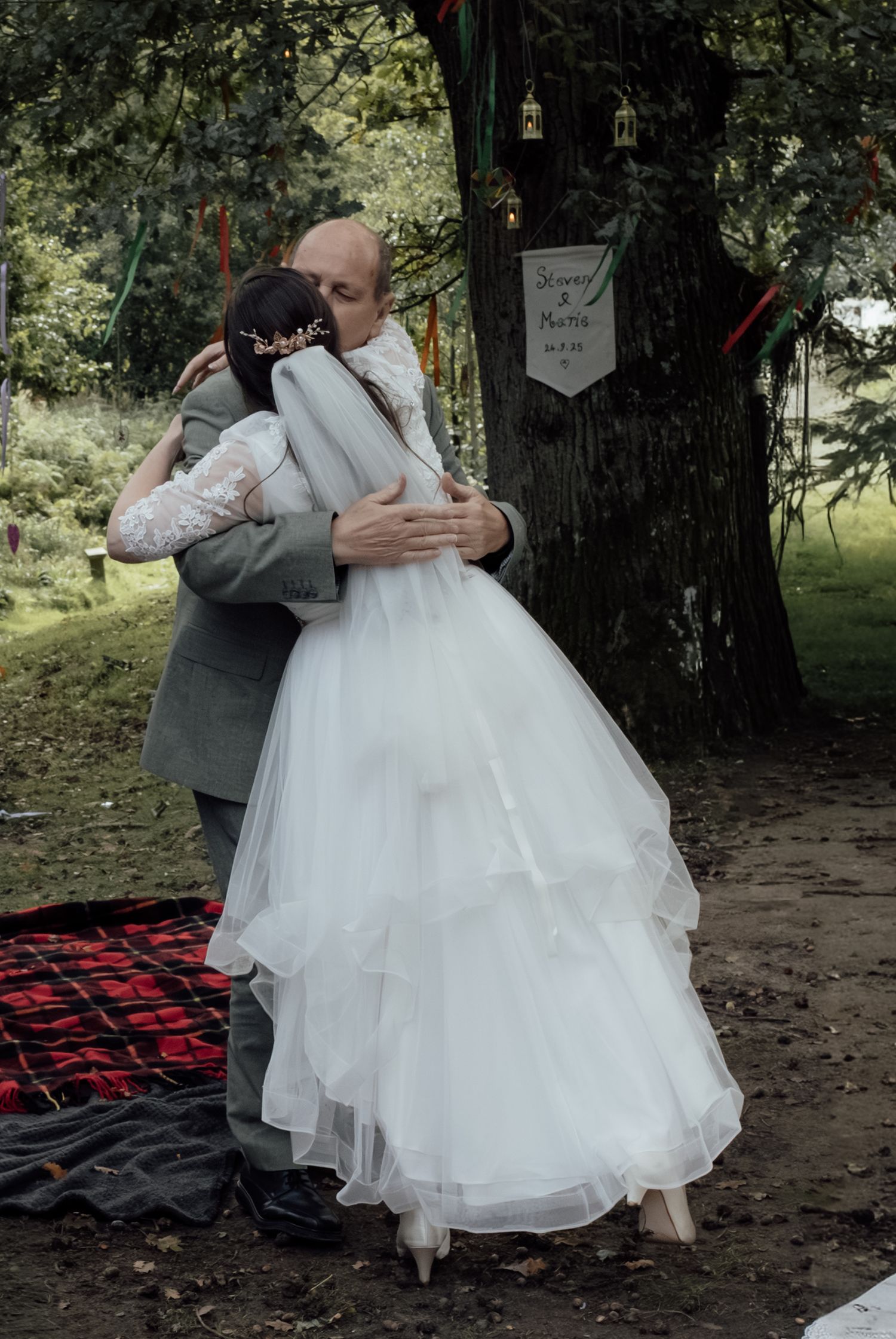 A couple shares an intimate embrace during their outdoor wedding ceremony with a rustic woodland backdrop.