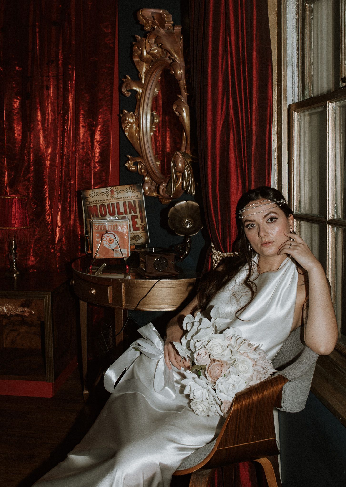 Dramatic wedding scene with red velvet curtains and white satin dress against vintage decor.