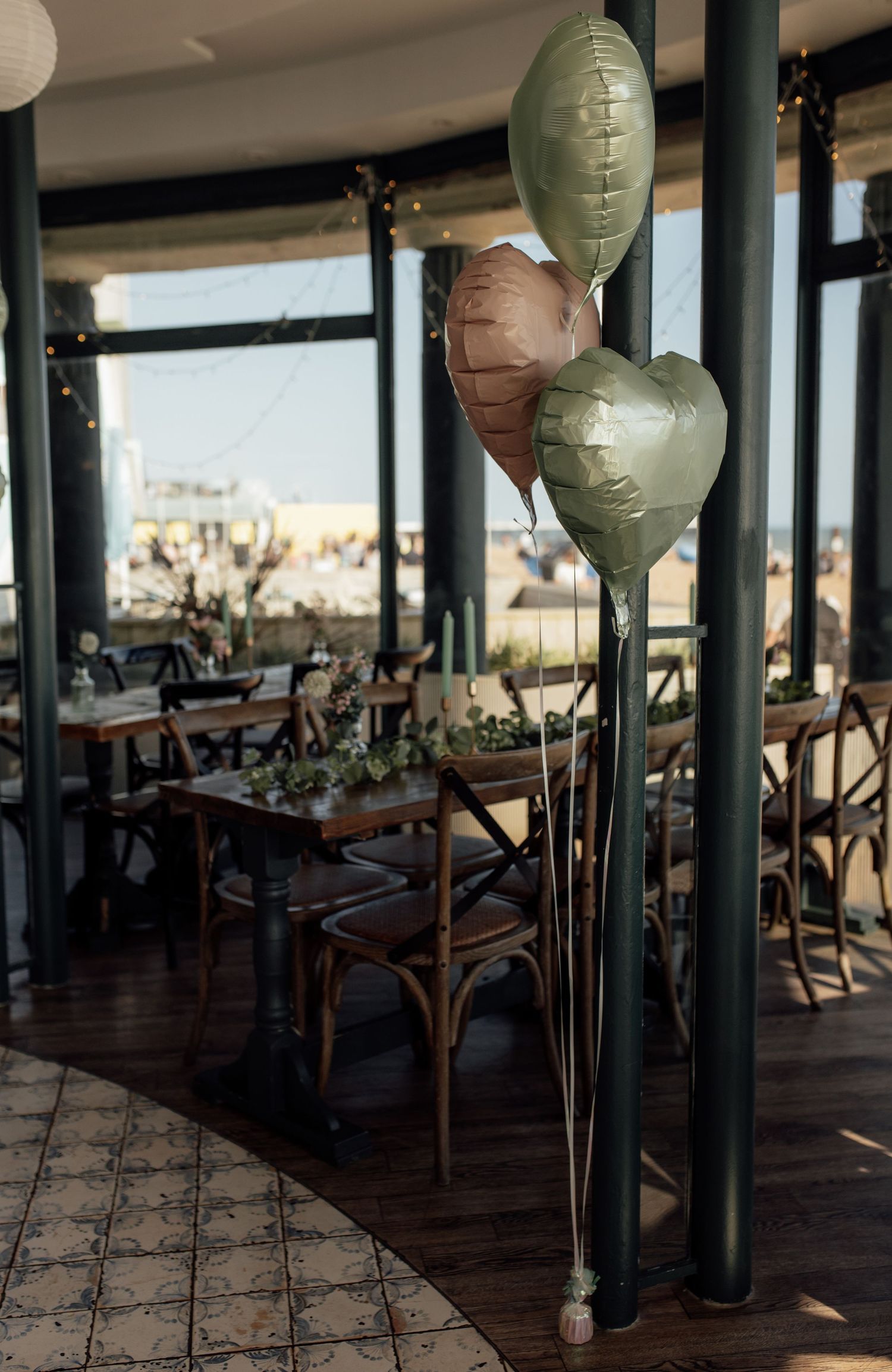 Elegant restaurant interior with green columns and balloon decorations overlooking a cityscape through large windows.