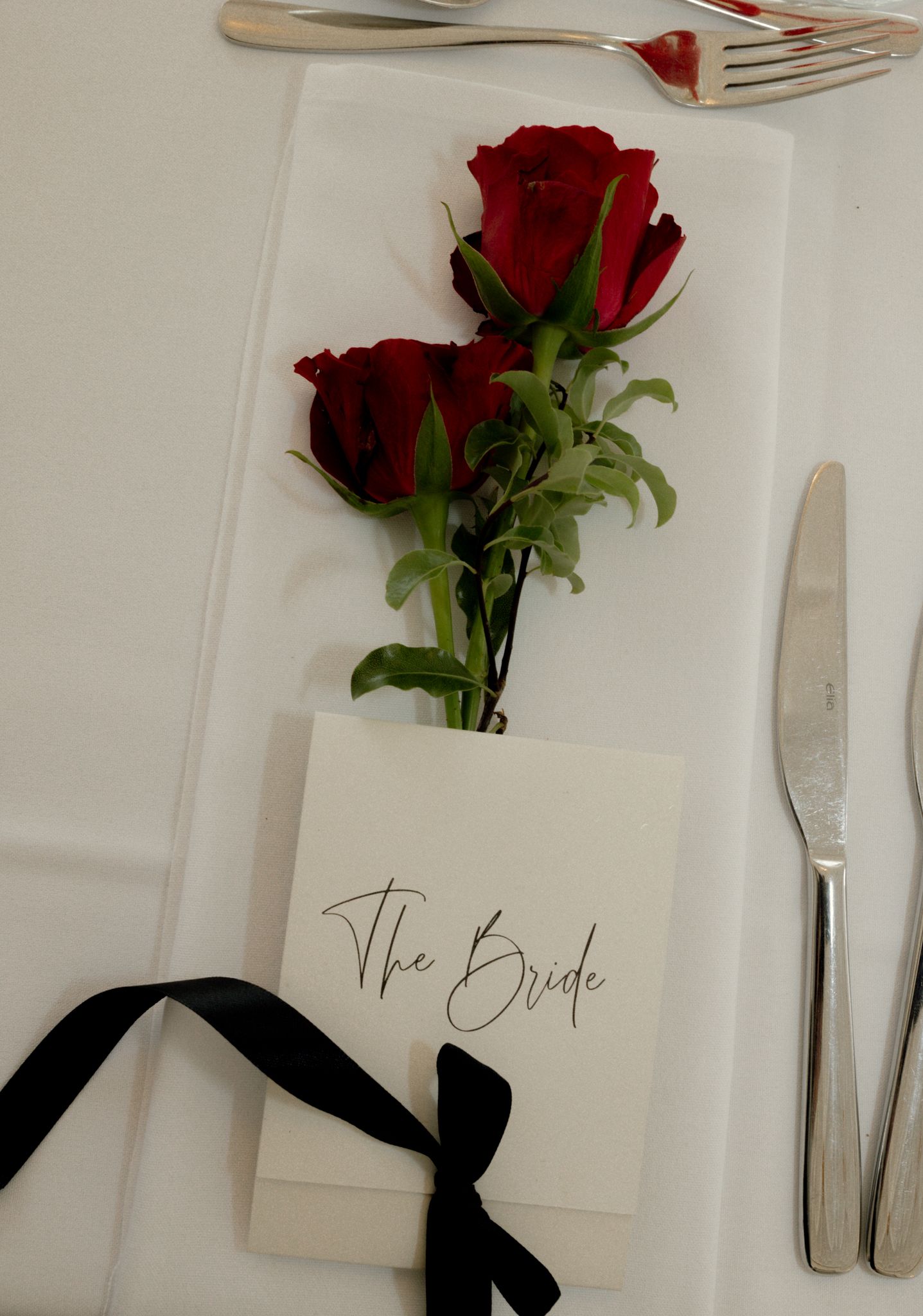 Wedding place setting with red roses and elegant calligraphy name card on white background.