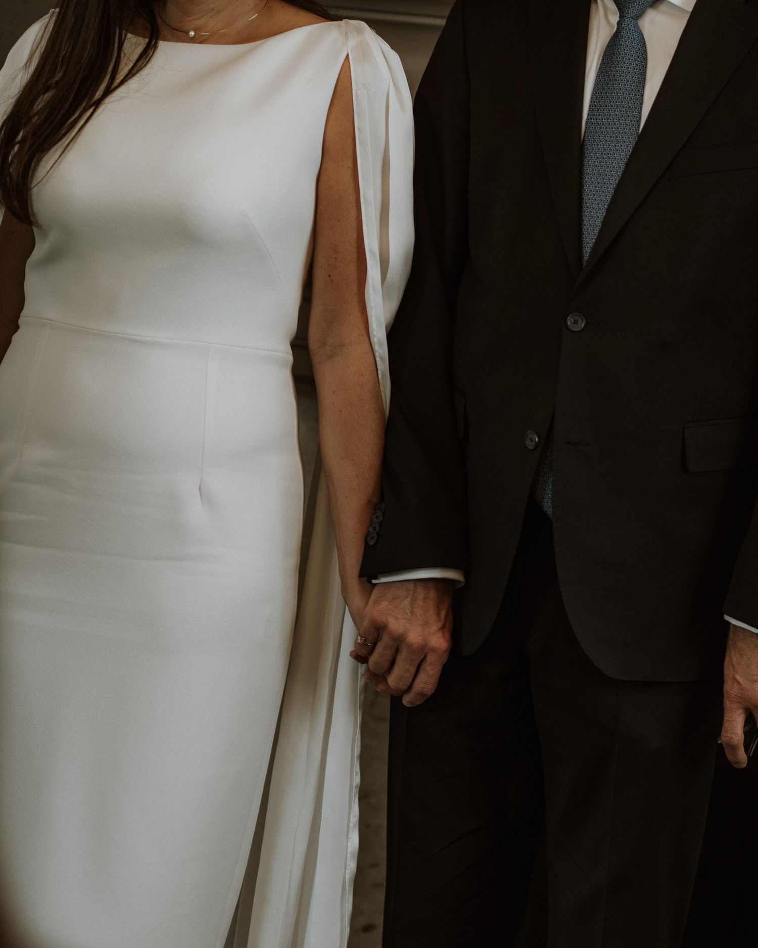 Elegant couple's formal attire shown from neck down, featuring white dress and dark suit.