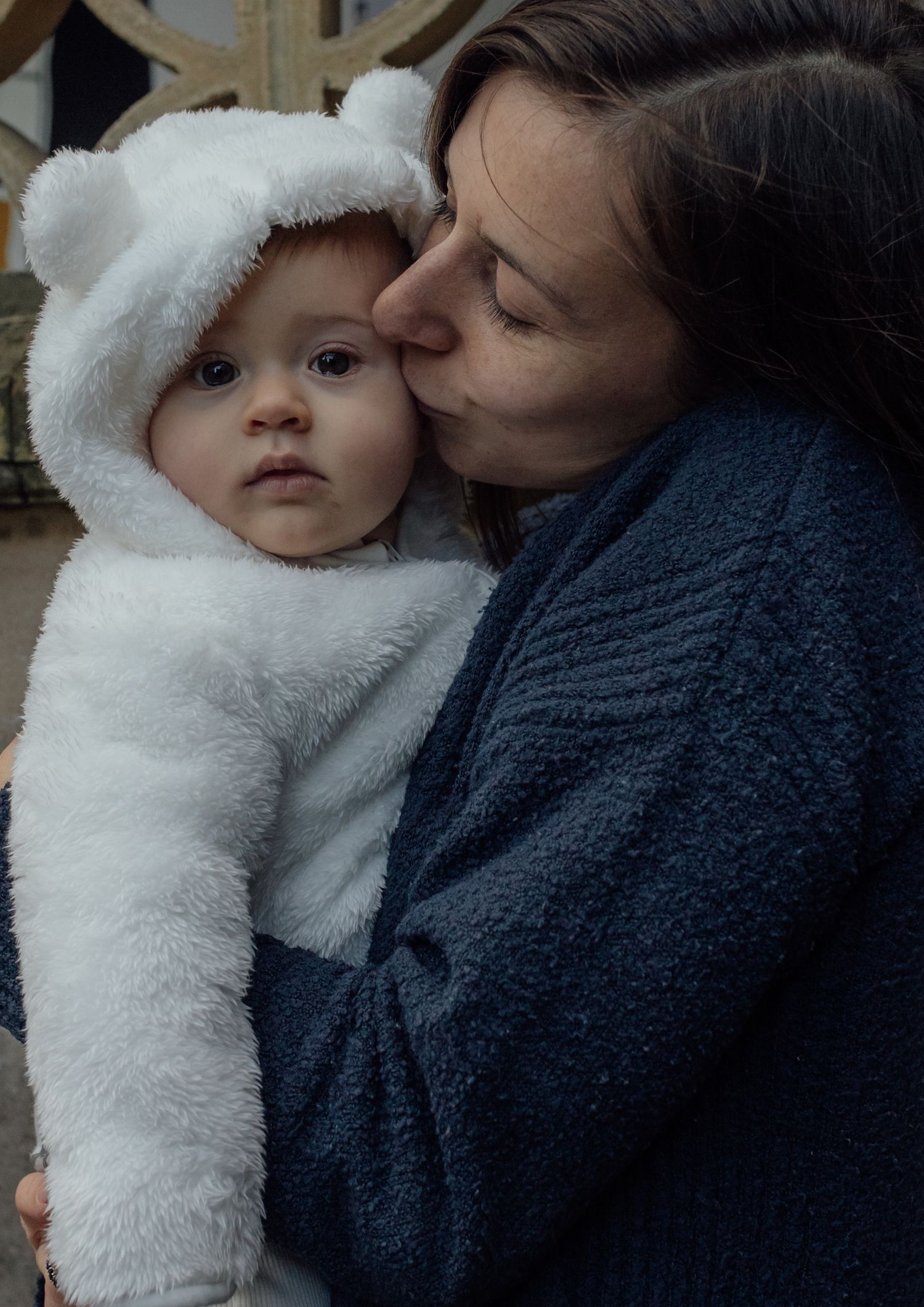 A tender moment between parent and baby wearing a fluffy white winter outfit with bear ears.