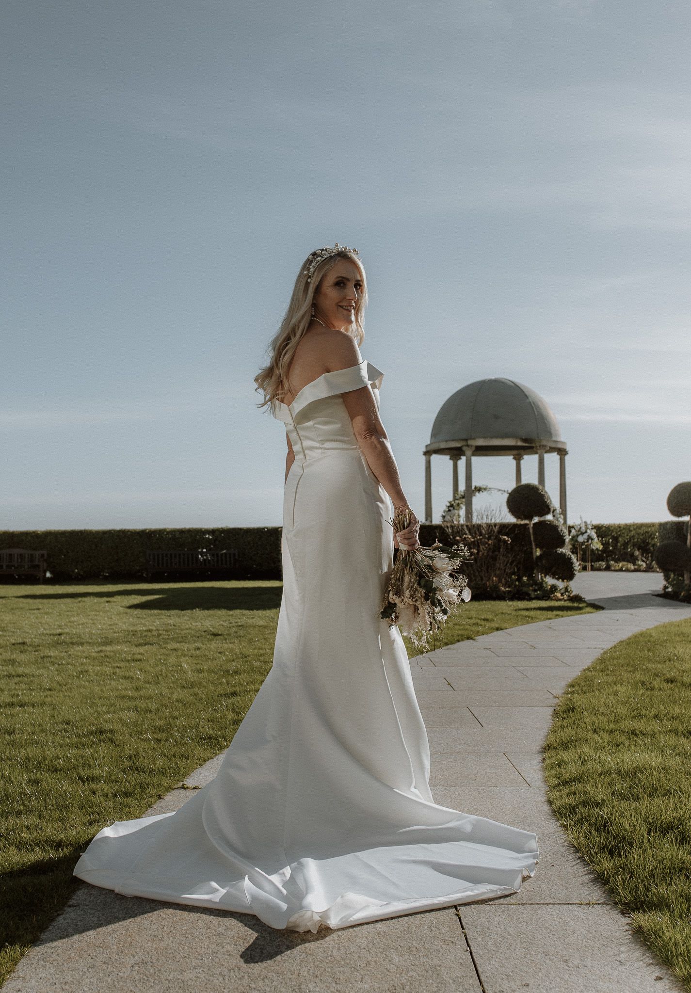 Ethereal wedding dress flows gracefully along a winding concrete path on a breezy day with an observatory in the background.