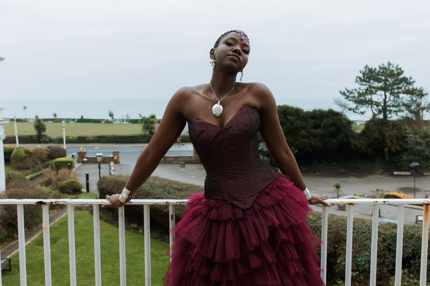 A person in a burgundy dress stands outdoors in various scenic locations for a photo series.