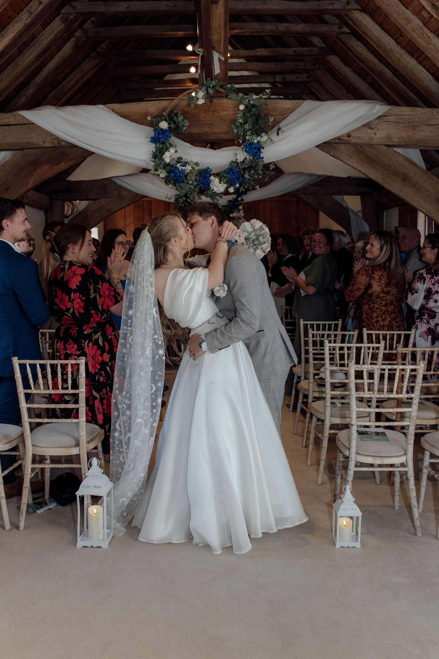Wedding couple shares intimate moments during their rustic barn ceremony with white chairs and blue floral decor.