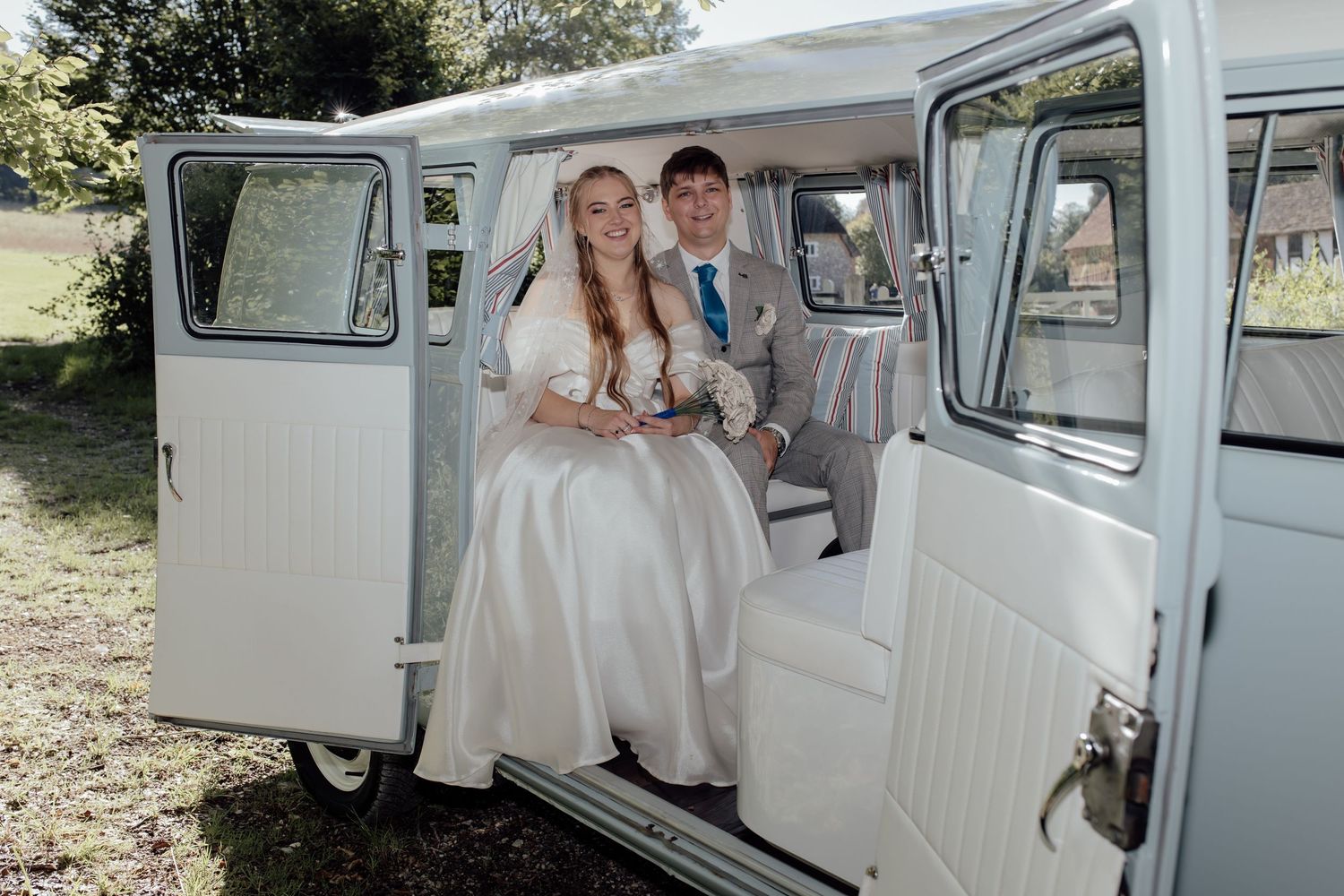 A vintage white Volkswagen van serves as a charming backdrop for wedding photos in a rustic outdoor setting.