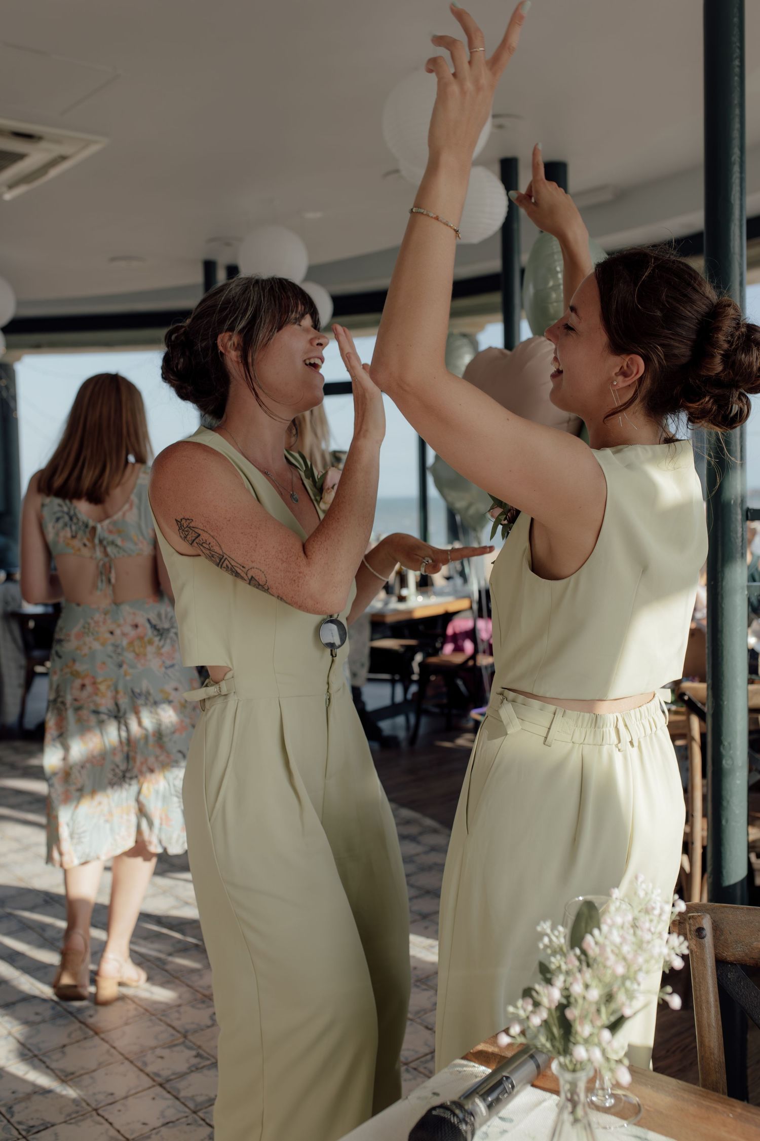 Wedding party guests in light green dresses dance and celebrate together at an indoor reception venue.