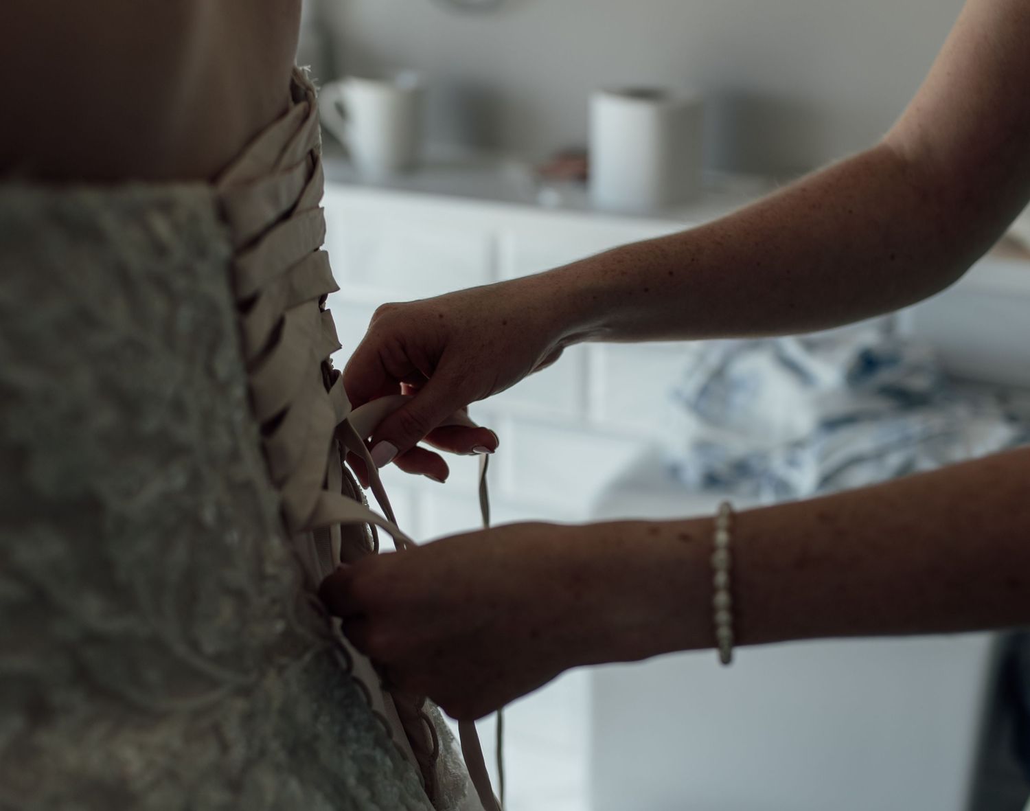 Close-up shot of hands carefully cutting into a white wedding cake with a silver knife.