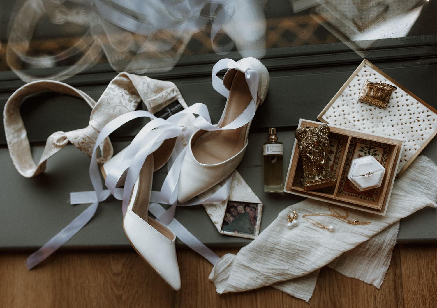 Wedding details flat lay with white heels, jewelry box and fabric on wooden surface.