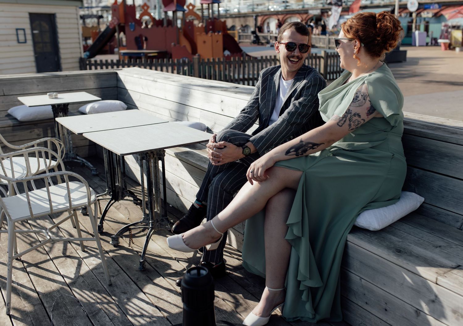 People sitting at outdoor metal tables and chairs on a patio area in an urban setting.