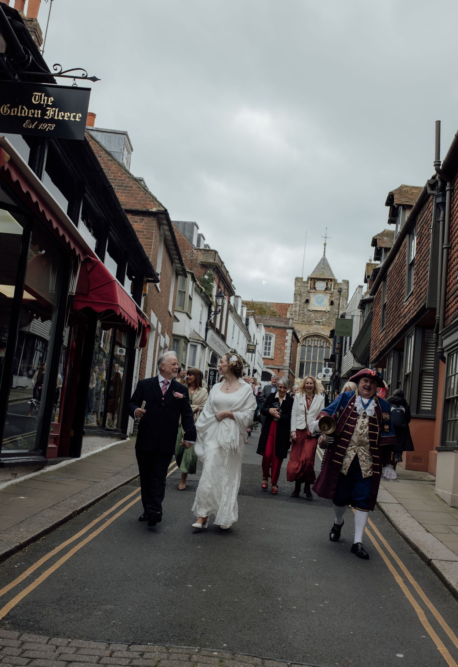 Bride and Groom walk down the road with town crier taking them to their reception.