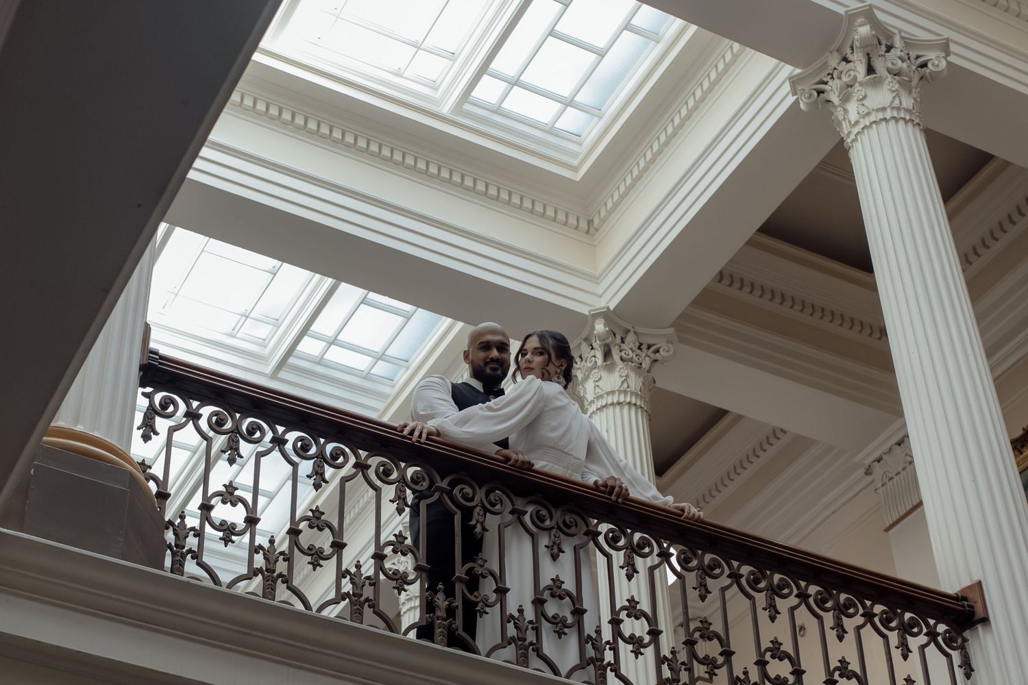 Interior view of a grand historic building with white columns and ornate balcony railings lit by natural skylights.
