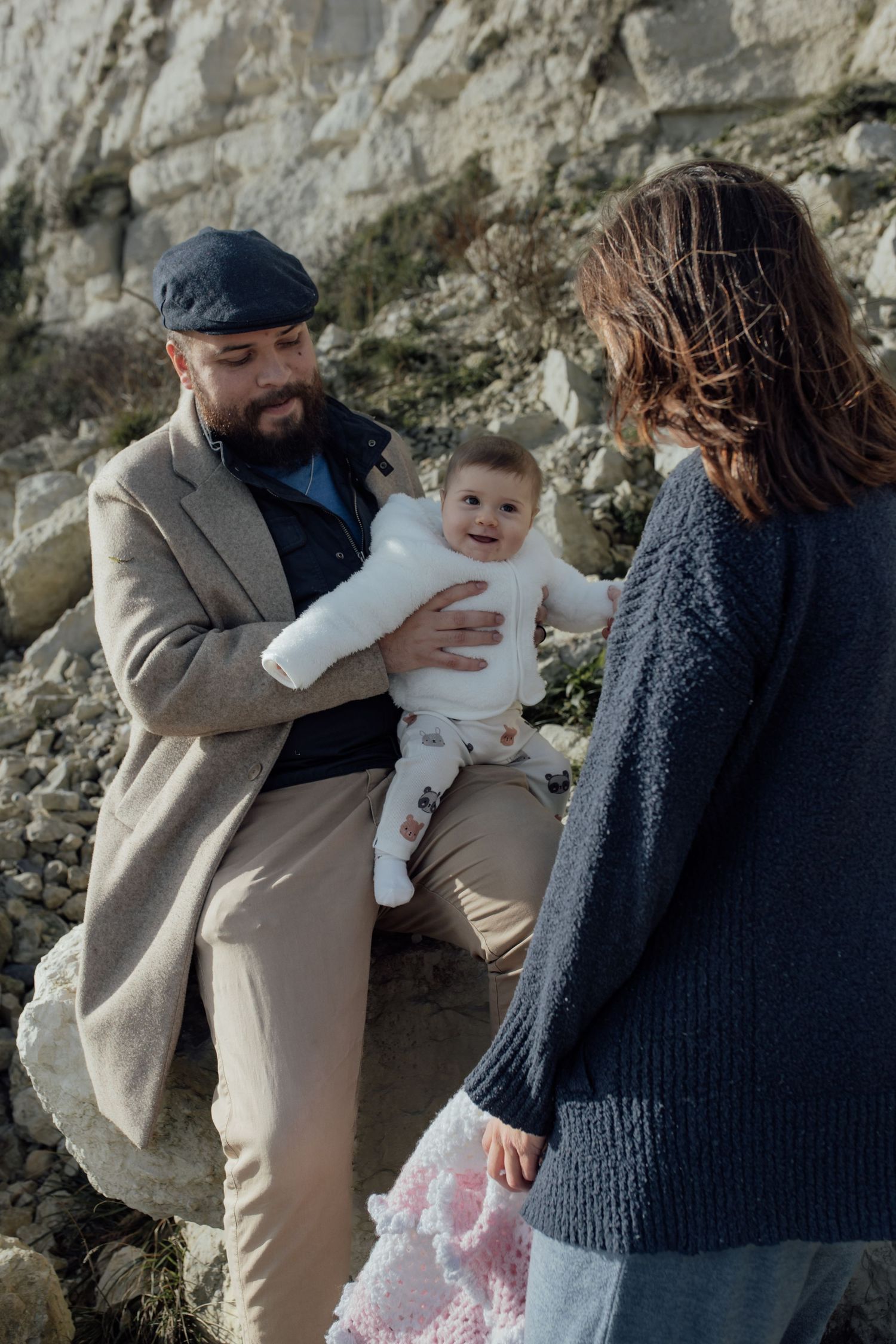 A series of candid family photos showing tender moments between parents and a baby against a stone wall backdrop.