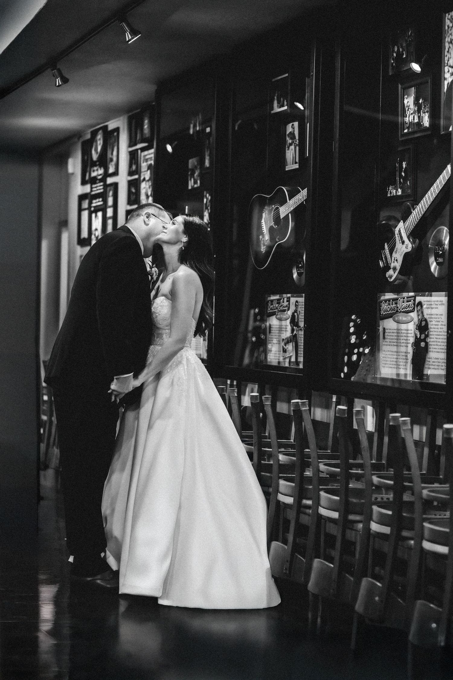 “Black and white portrait of a groom leaning in and kissing the bride’s neck as they stand together.”