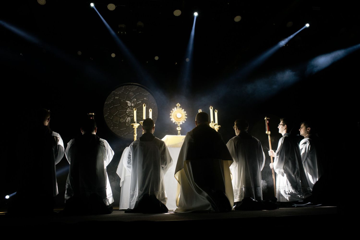 Silhouettes of religious figures stand dramatically backlit in darkness.