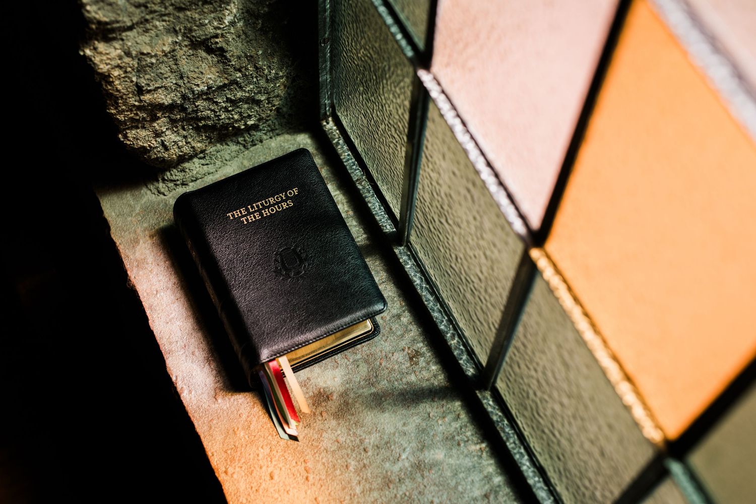 A small black leather Bible resting on a colorful tiled surface in dramatic lighting.