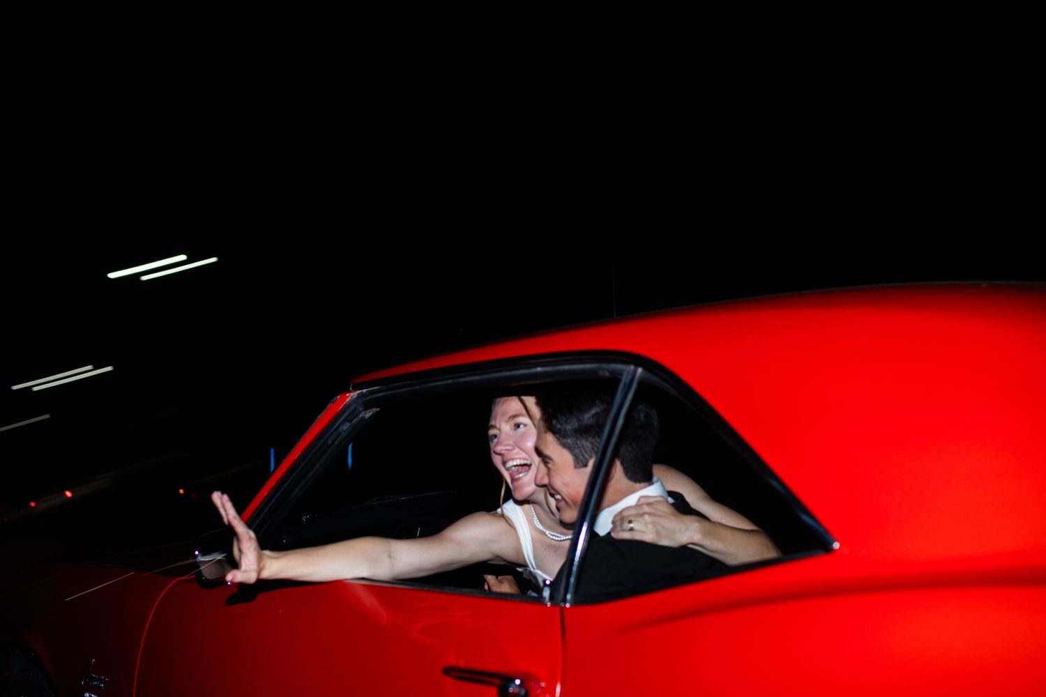 A bright red classic car with someone posing through the driver's side window at night.