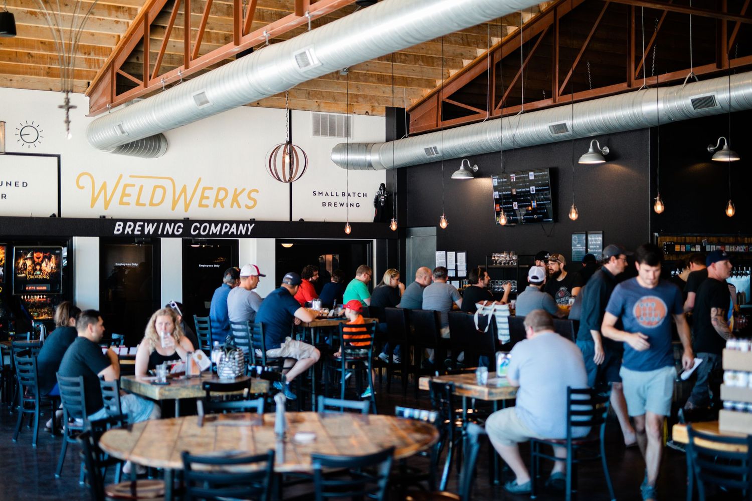Wide interior view of a bustling brewery taproom with exposed ceiling and industrial design elements.