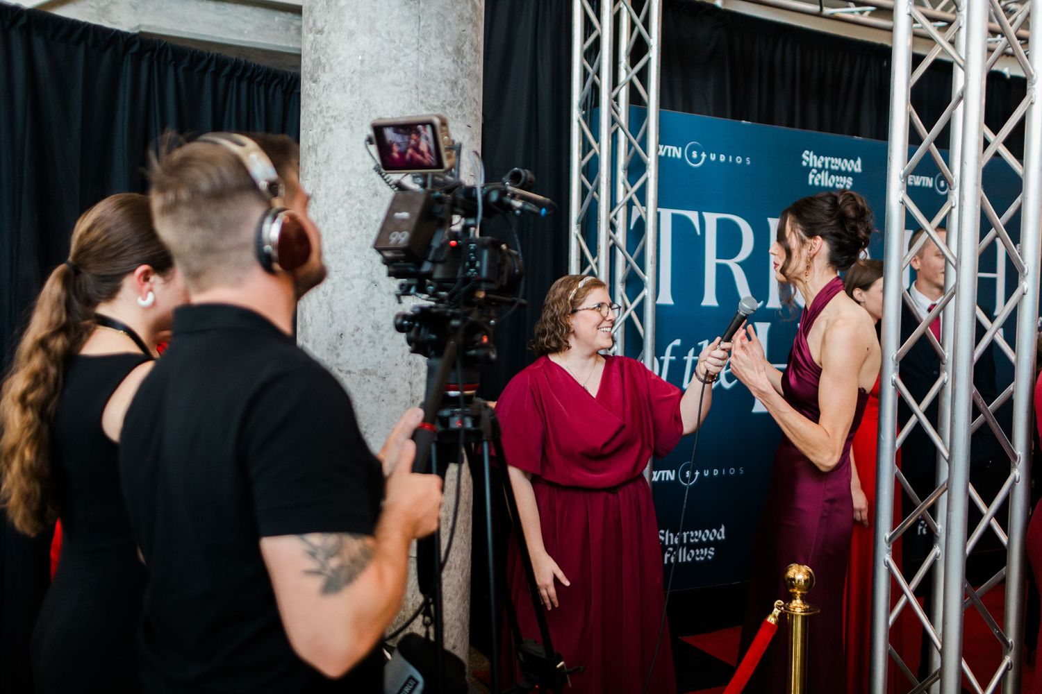Professional camera operators and crew members film an event in a venue with stage lighting and equipment.