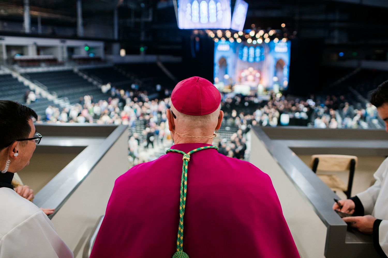 Cardinals in red robes seated at a church gathering viewed from behind.