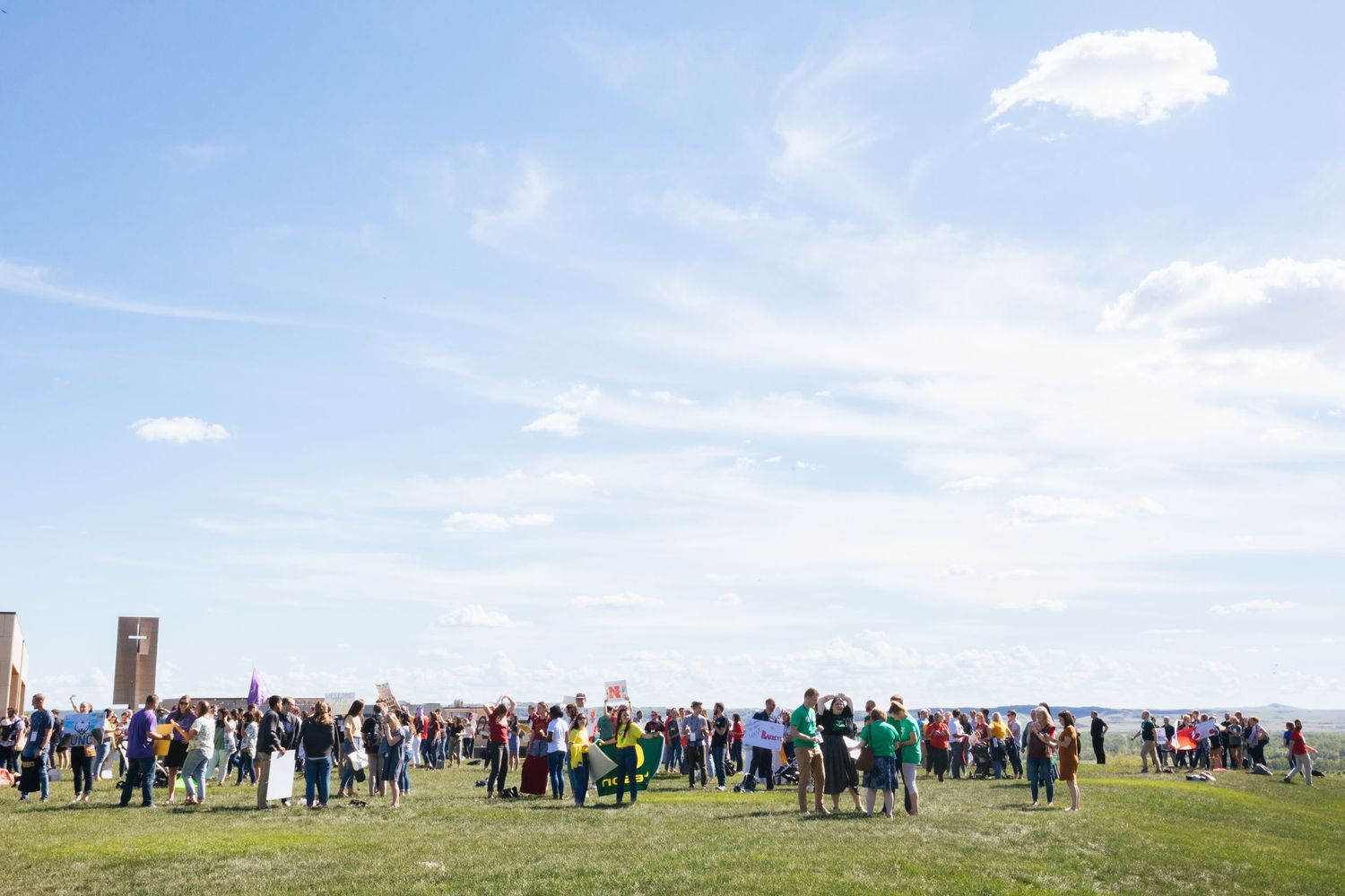 A large crowd of spectators gathers on a grassy hilltop under blue skies to watch an outdoor event.