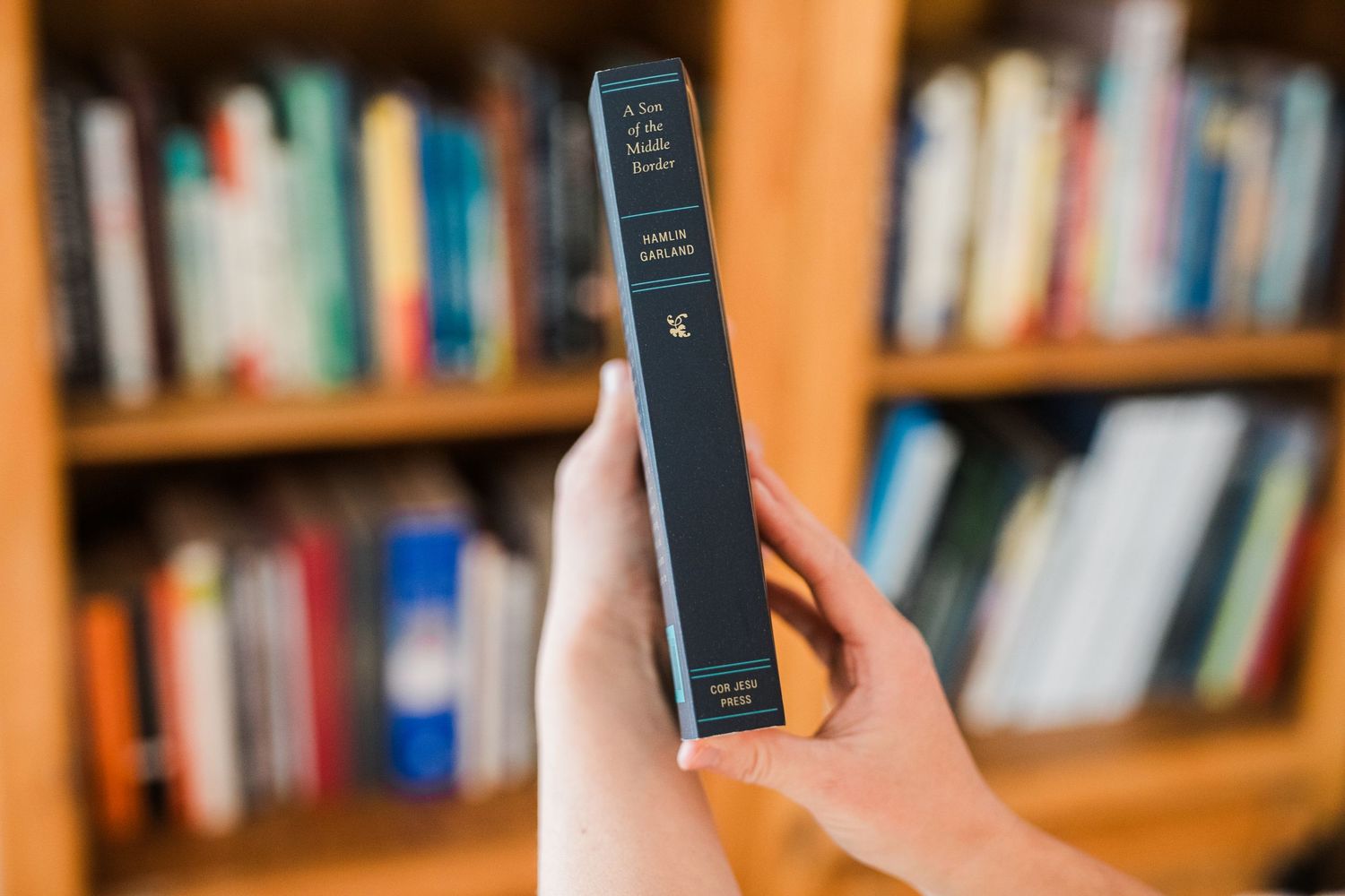 Hand holding a black smartphone against a blurry bookshelf background in a library or study.