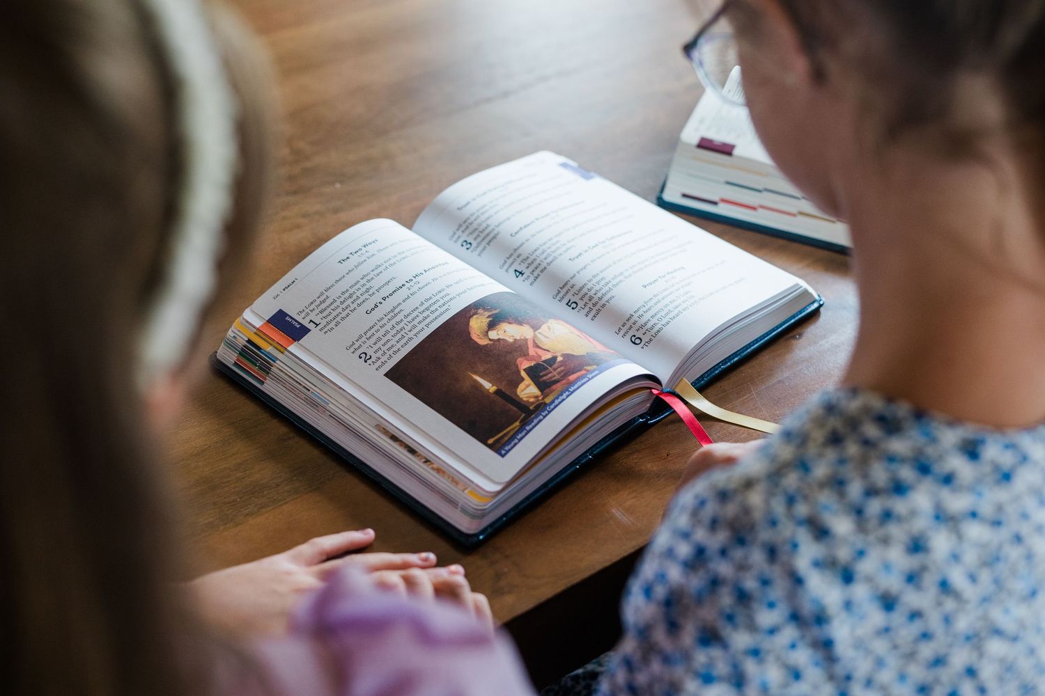 Two students studying an illustrated textbook together at a wooden desk.