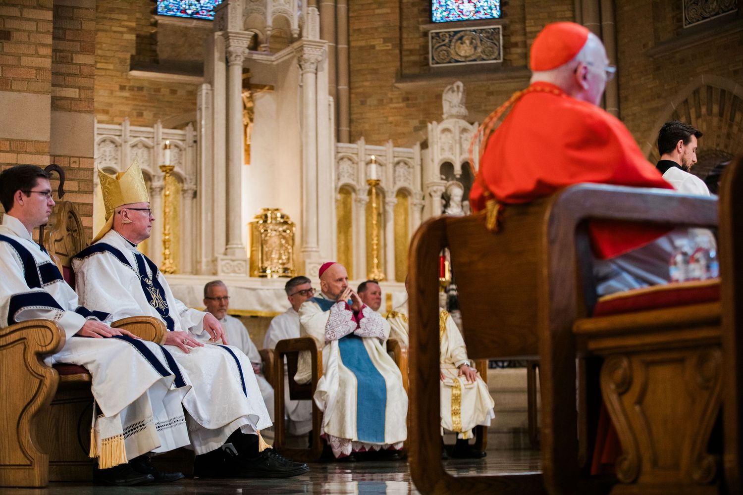 Cardinal and bishops in ceremonial vestments seated during Catholic Mass in ornate cathedral.