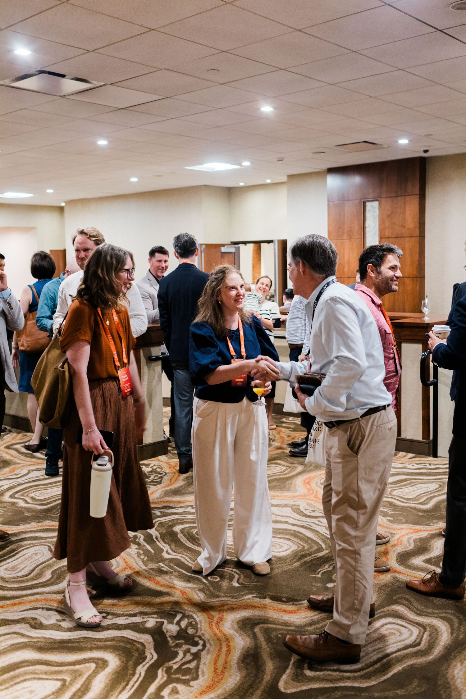 Professionals networking at a conference reception in a hotel ballroom, engaging in conversation on a patterned carpet.
