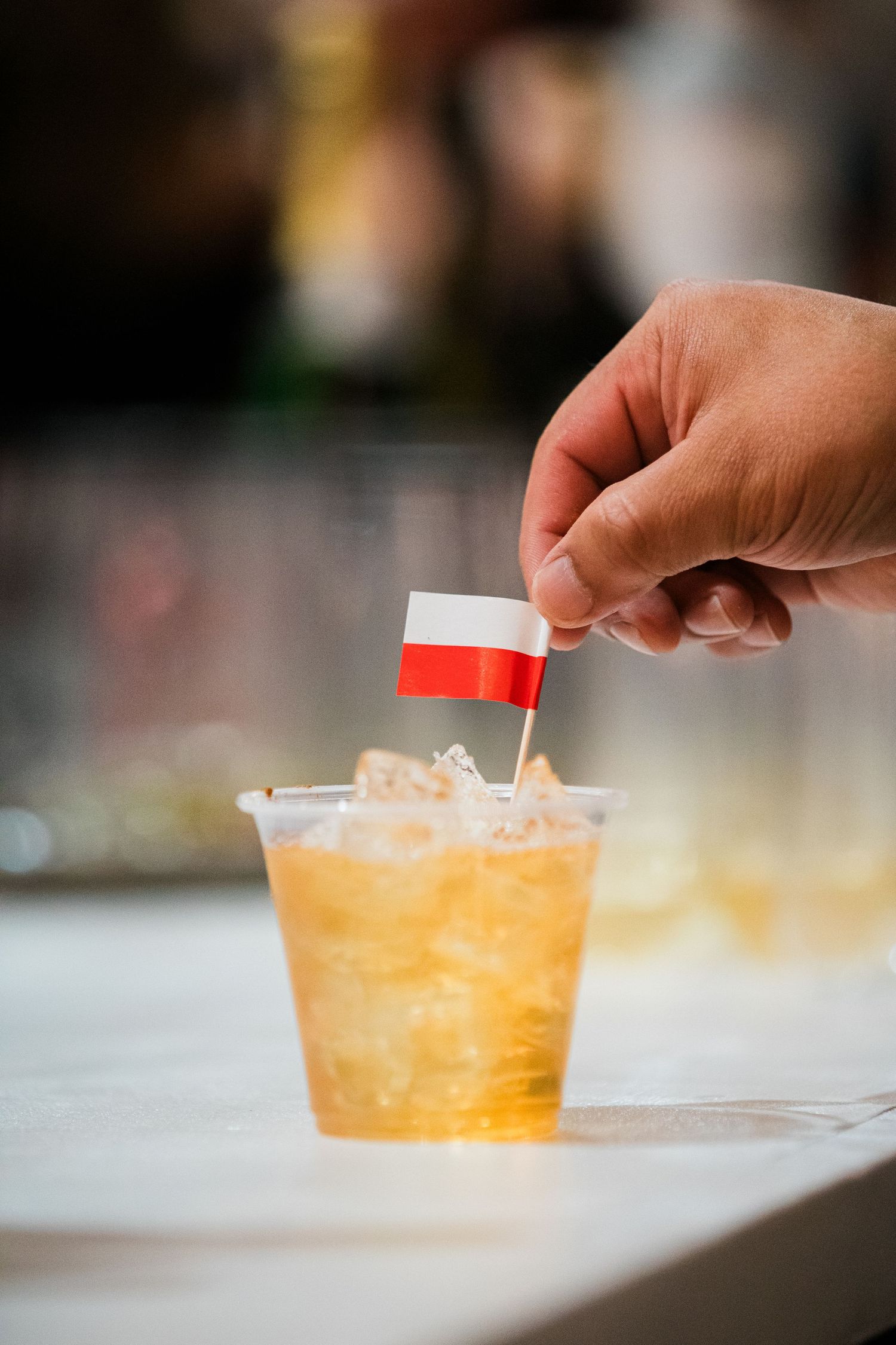 A hand places a small Polish flag into a golden cocktail filled with ice.