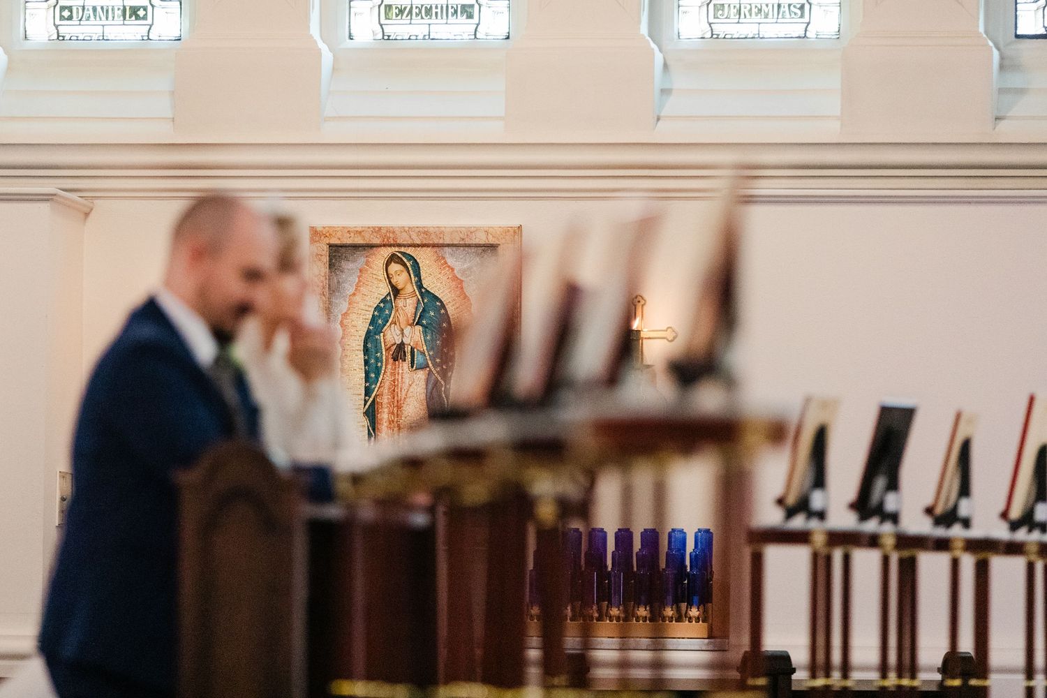 Man at podium in church with Our Lady of Guadalupe icon and candles in background during ceremony.
