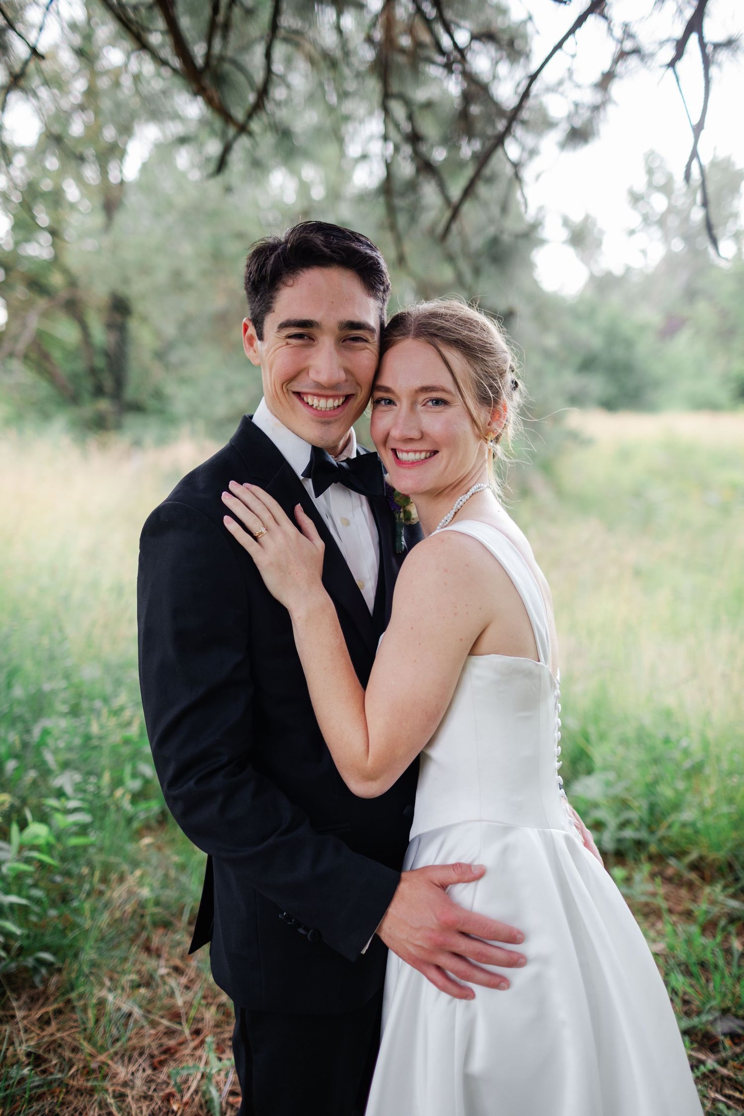 Romantic wedding couple embraces in a natural outdoor setting with tall grass and trees.