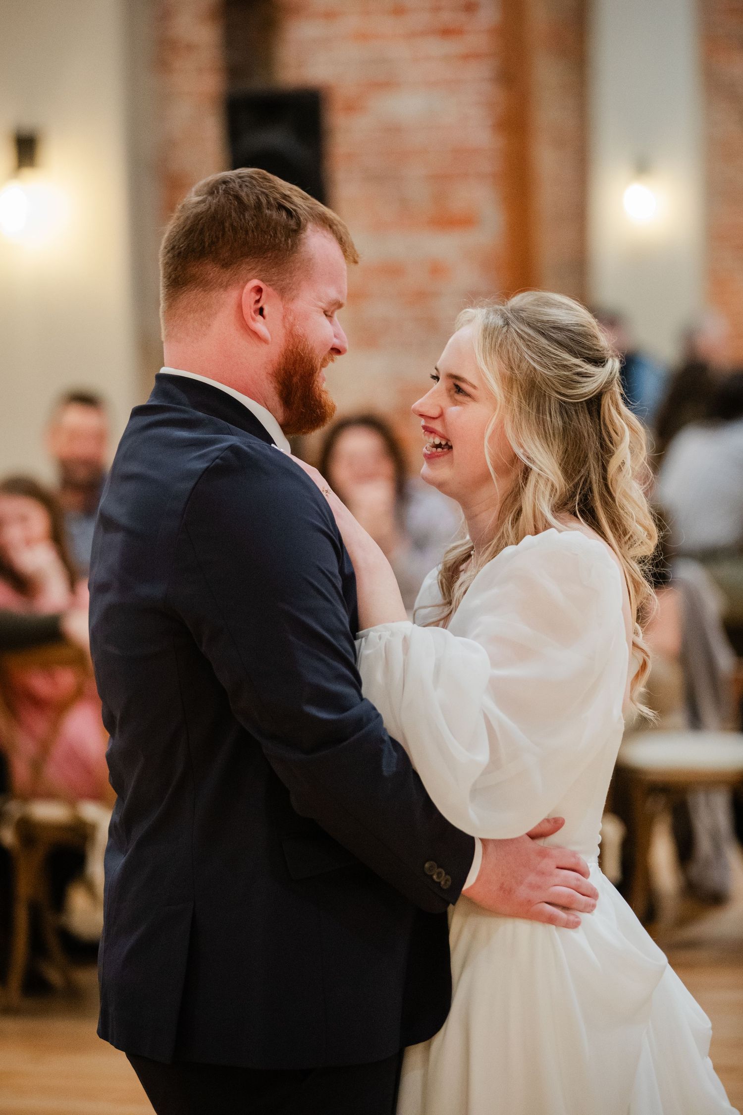 A couple shares a joyful dance moment in a venue with exposed brick walls and warm lighting.