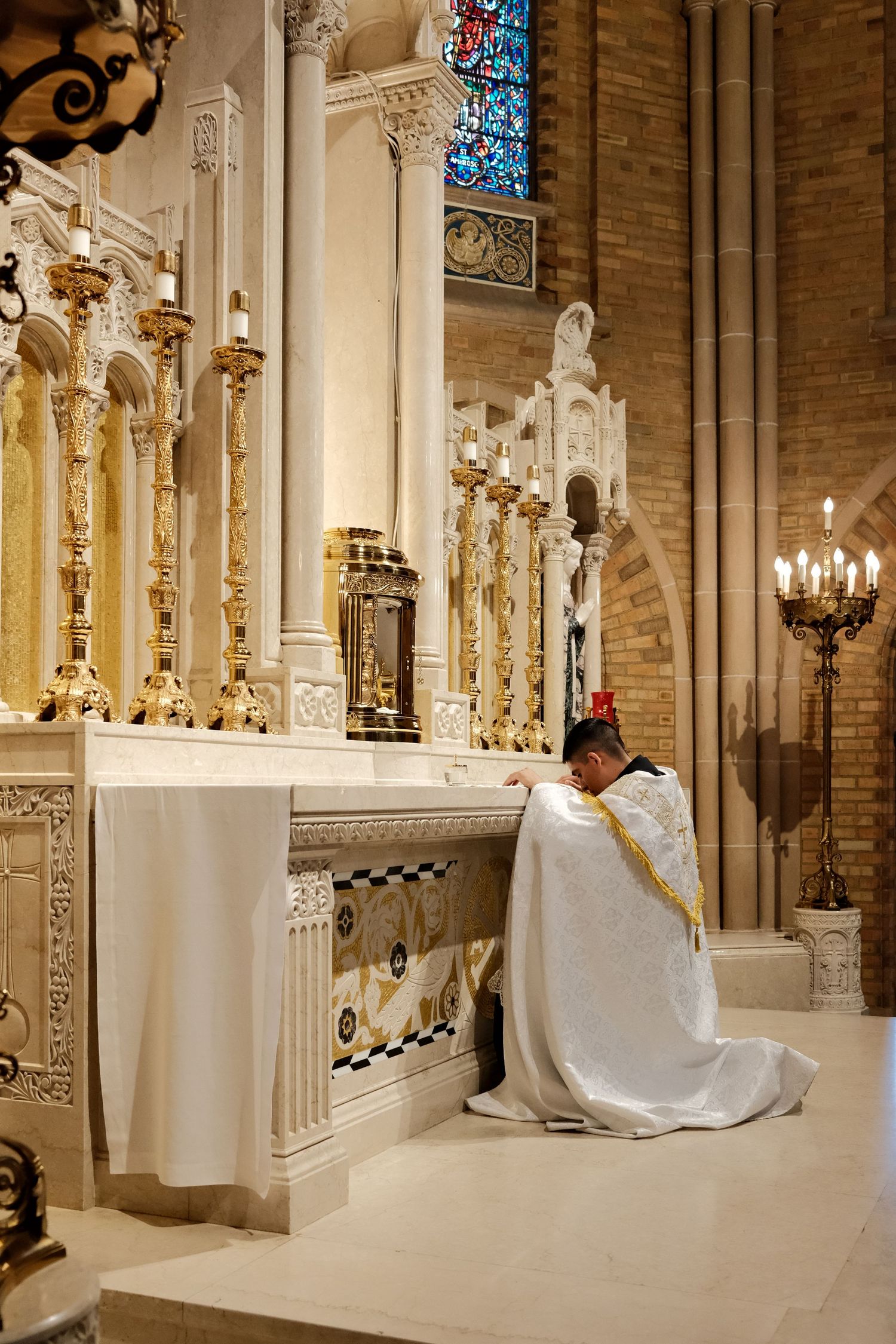A panoramic view of an ornate church altar with white marble columns, stained glass windows, and candlelit chandeliers.