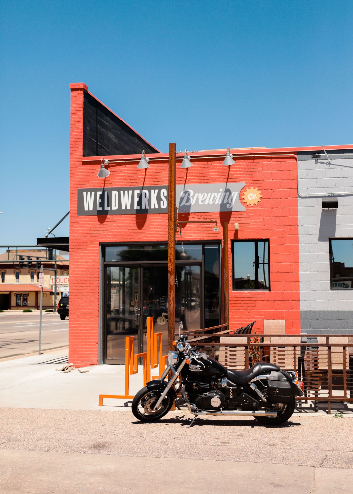 Red brick brewery building exterior with motorcycles parked outside under bright blue sky.