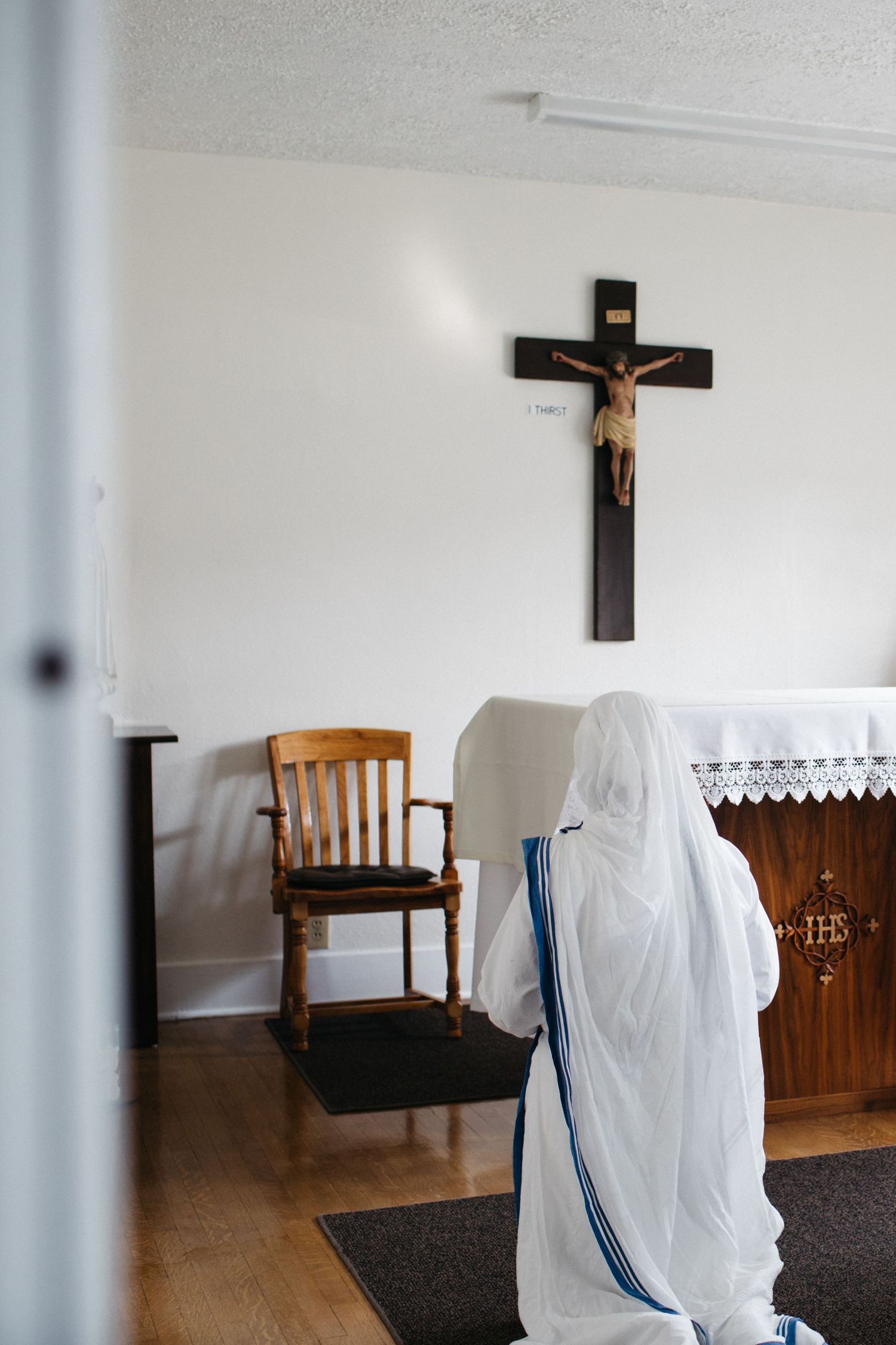 Simple church interior with wooden chairs, white walls, and crucifix on display.