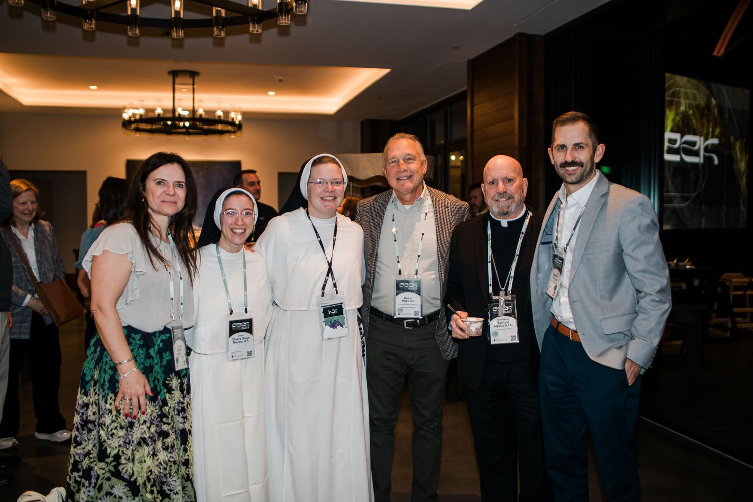 A group of conference attendees and religious sisters pose together for a photo at an indoor event.