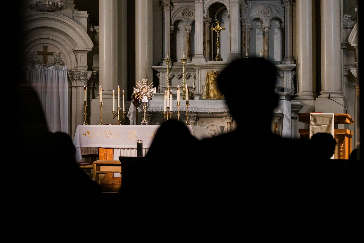 Silhouetted congregation seated before an ornate illuminated church altar during mass.