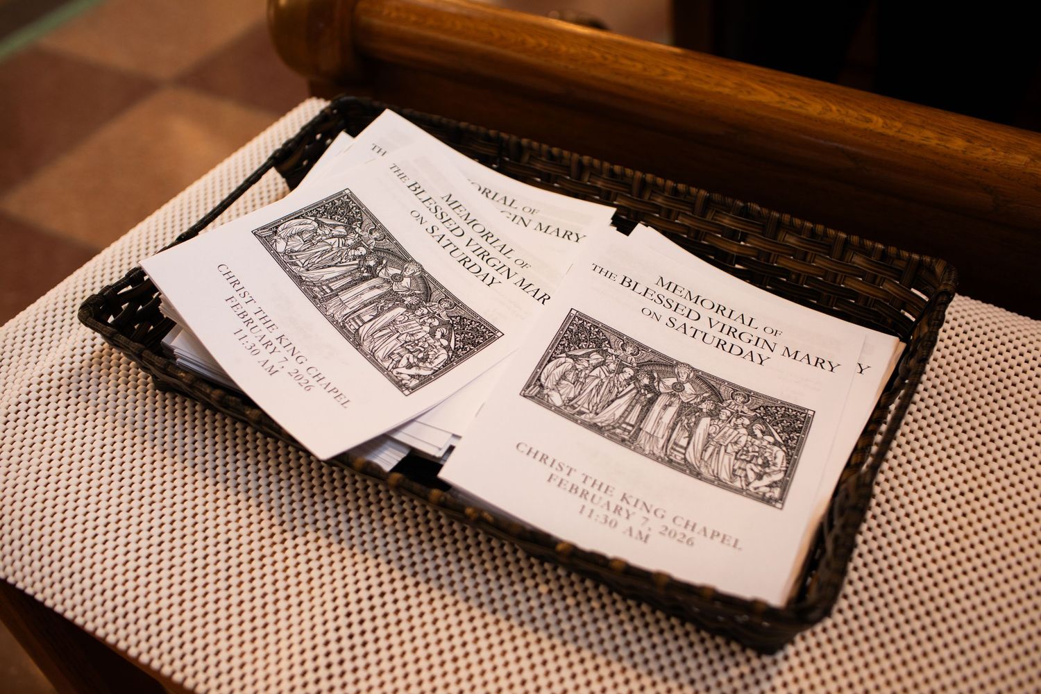 Mass missal booklets resting on a wooden church pew, featuring religious imagery and text for Catholic worship service.