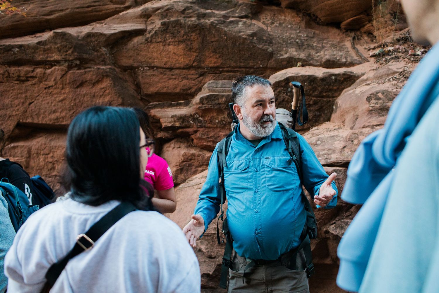 A group of hikers explore a red rock canyon formation with sandstone walls towering above them.